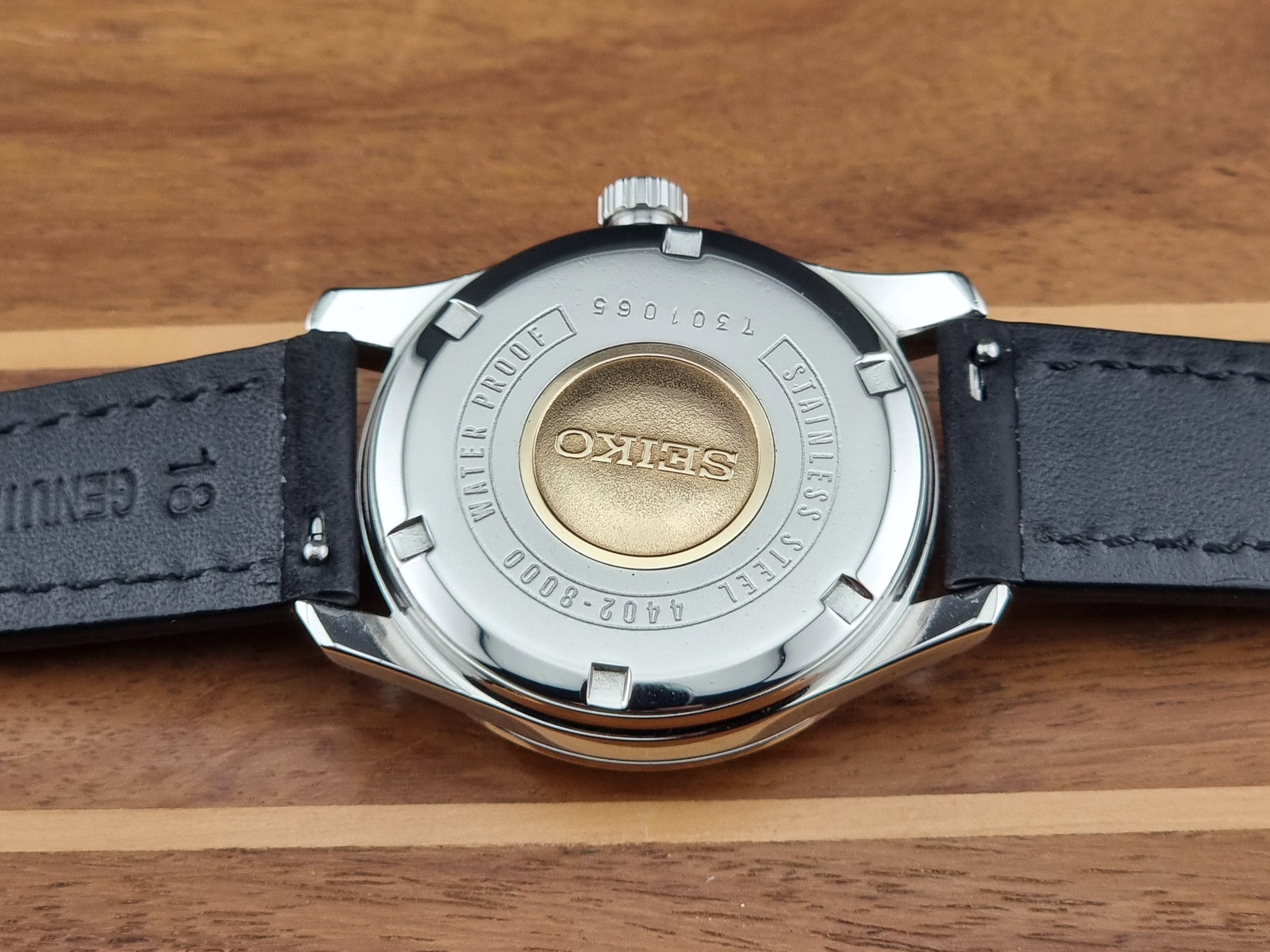 Vintage King Seiko 4402-8000 case back with black leather strap and visible brand logo on wooden surface