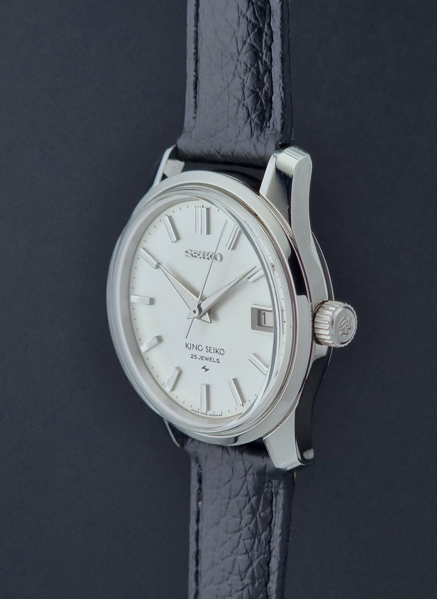 Vintage King Seiko Wristwatch 4402-8000 on a black leather strap on a dark background profile view crown side