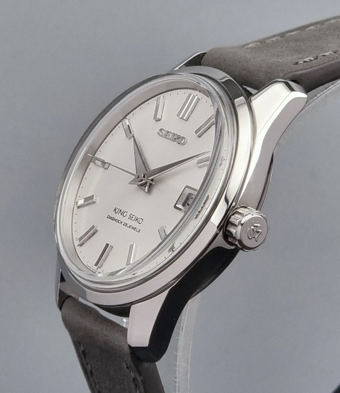 Vintage King Seiko 4402-8000 watch with a silver case and grey leather strap on a gray background side profile close up crown
