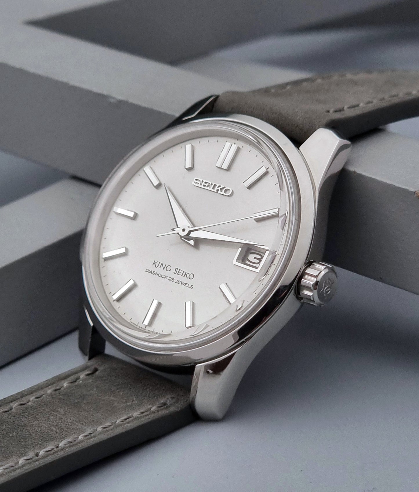Vintage King Seiko 4402-8000 watch with a silver case and grey leather strap on a gray background crown view