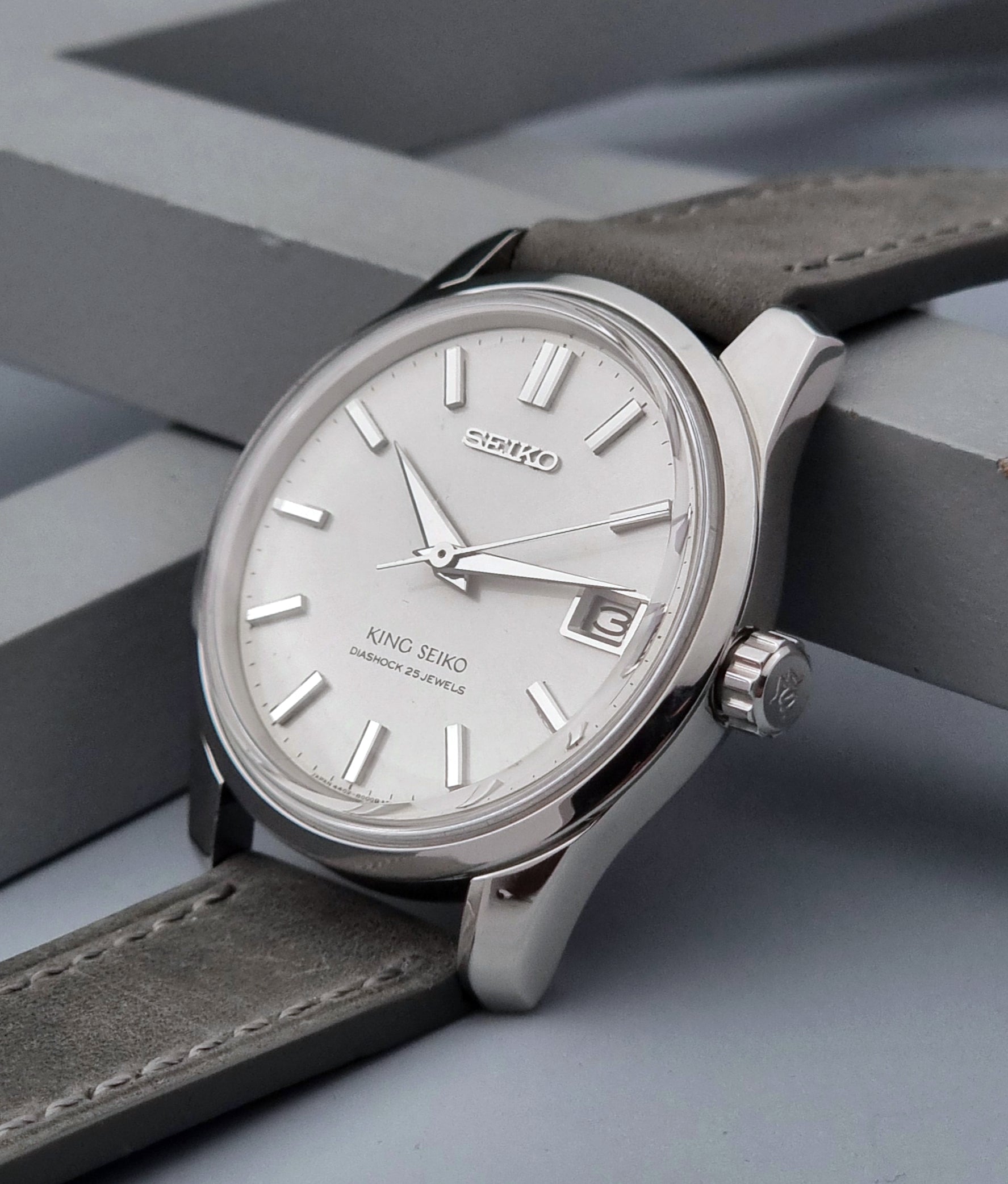 Vintage King Seiko 4402-8000 watch with a silver case and grey leather strap on a gray background crown view