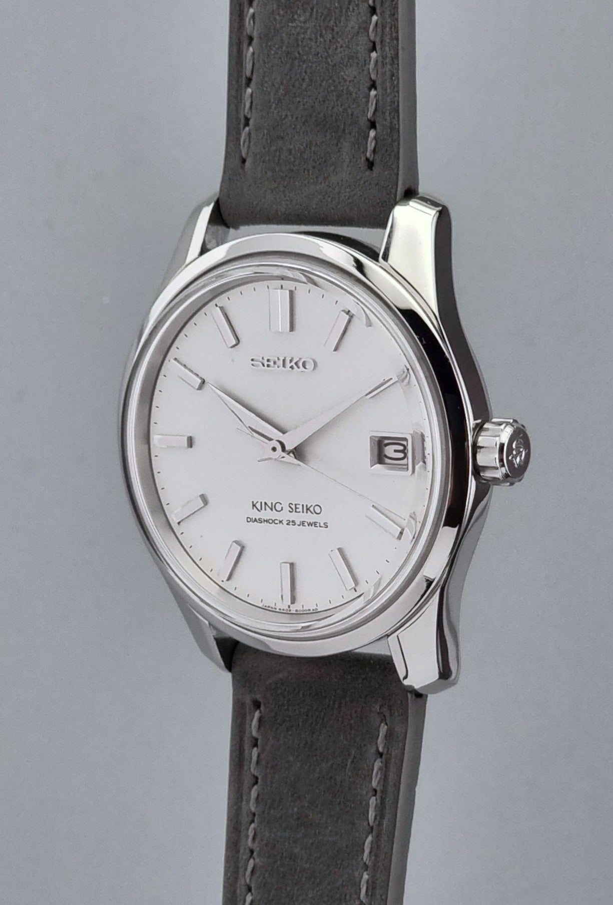 Vintage King Seiko 4402-8000 watch with a silver case and grey leather strap on a gray background side profile crown view