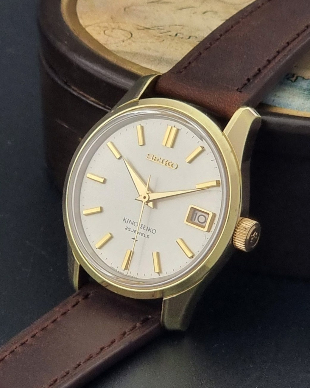 Vintage King Seiko 4402-8000 wristwatch with brown leather strap and gold case on a world map background crown view