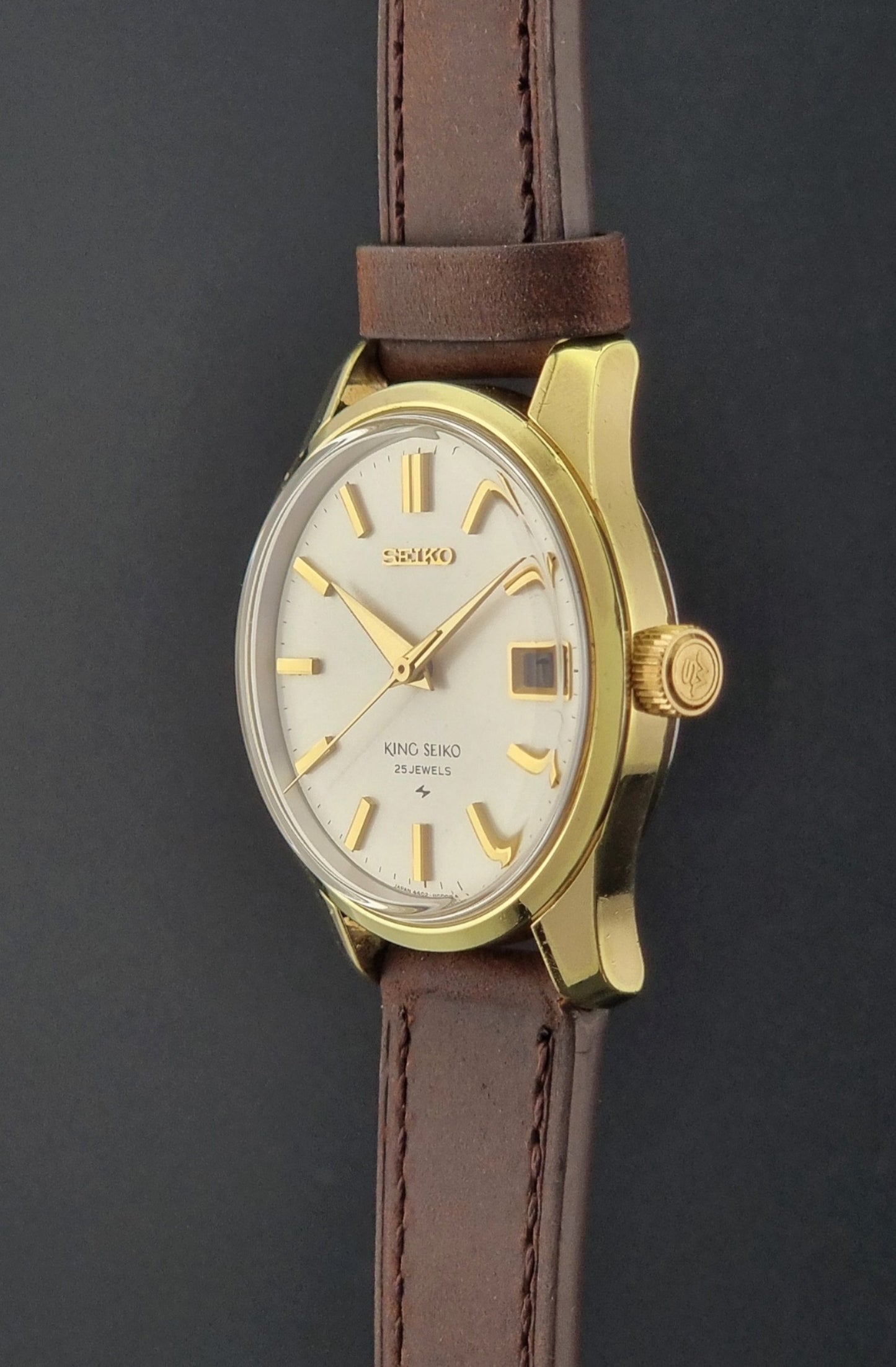 Vintage King Seiko 4402-8000 wristwatch with brown leather strap and gold case on a world map background side profile with crown