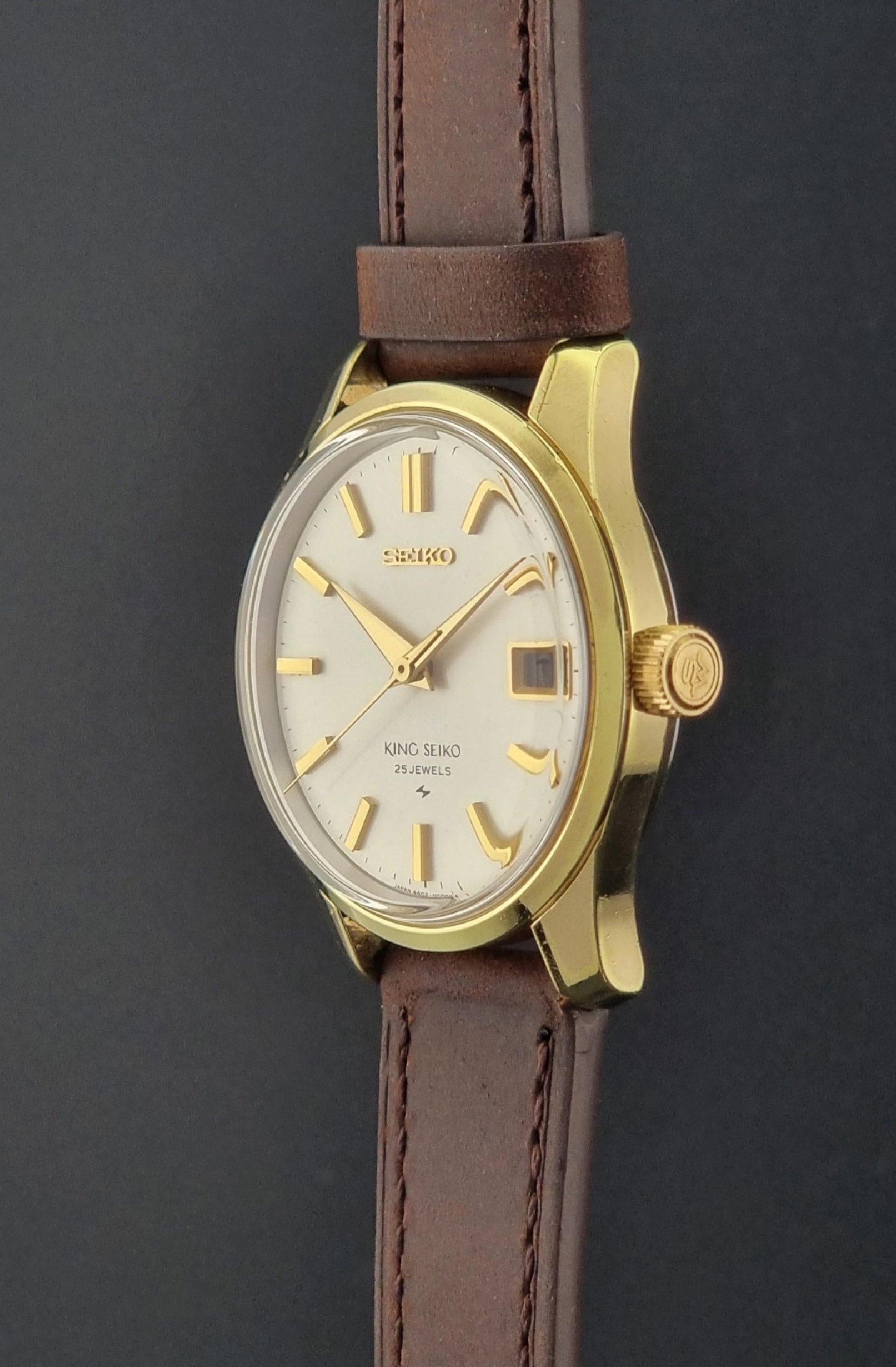Vintage King Seiko 4402-8000 wristwatch with brown leather strap and gold case on a world map background side profile with crown