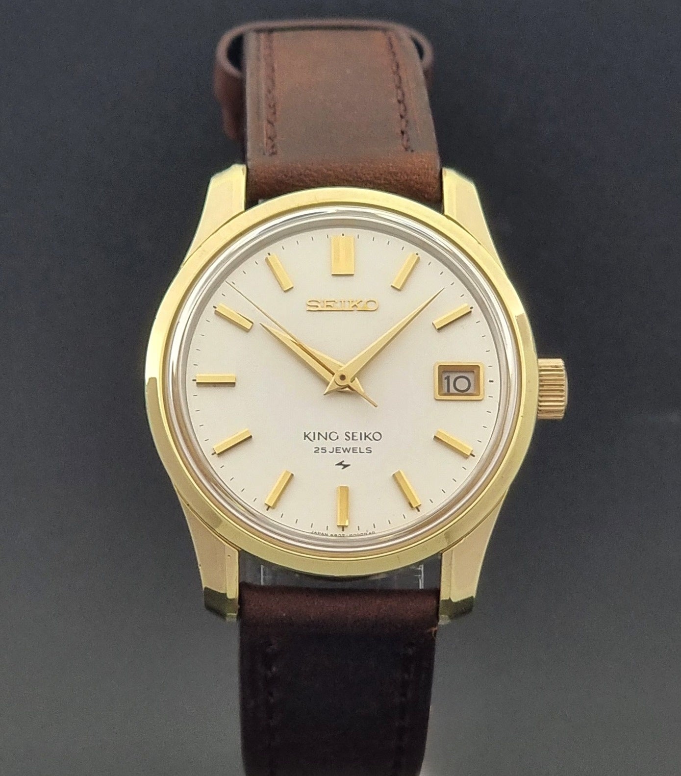 Vintage King Seiko 4402-8000 wristwatch with brown leather strap and gold case on a world map background close dial view