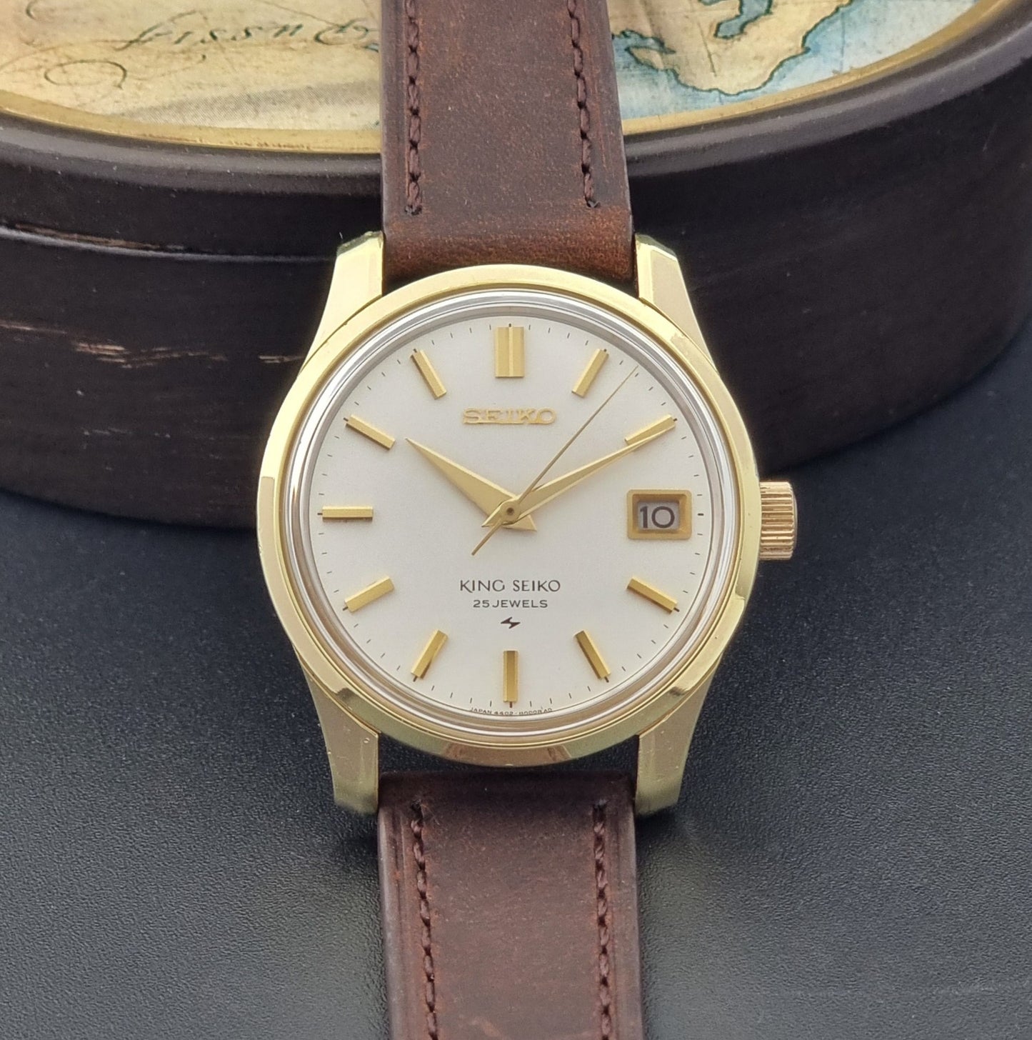 Vintage King Seiko 4402-8000 wristwatch with brown leather strap and gold case on a world map background dial view 