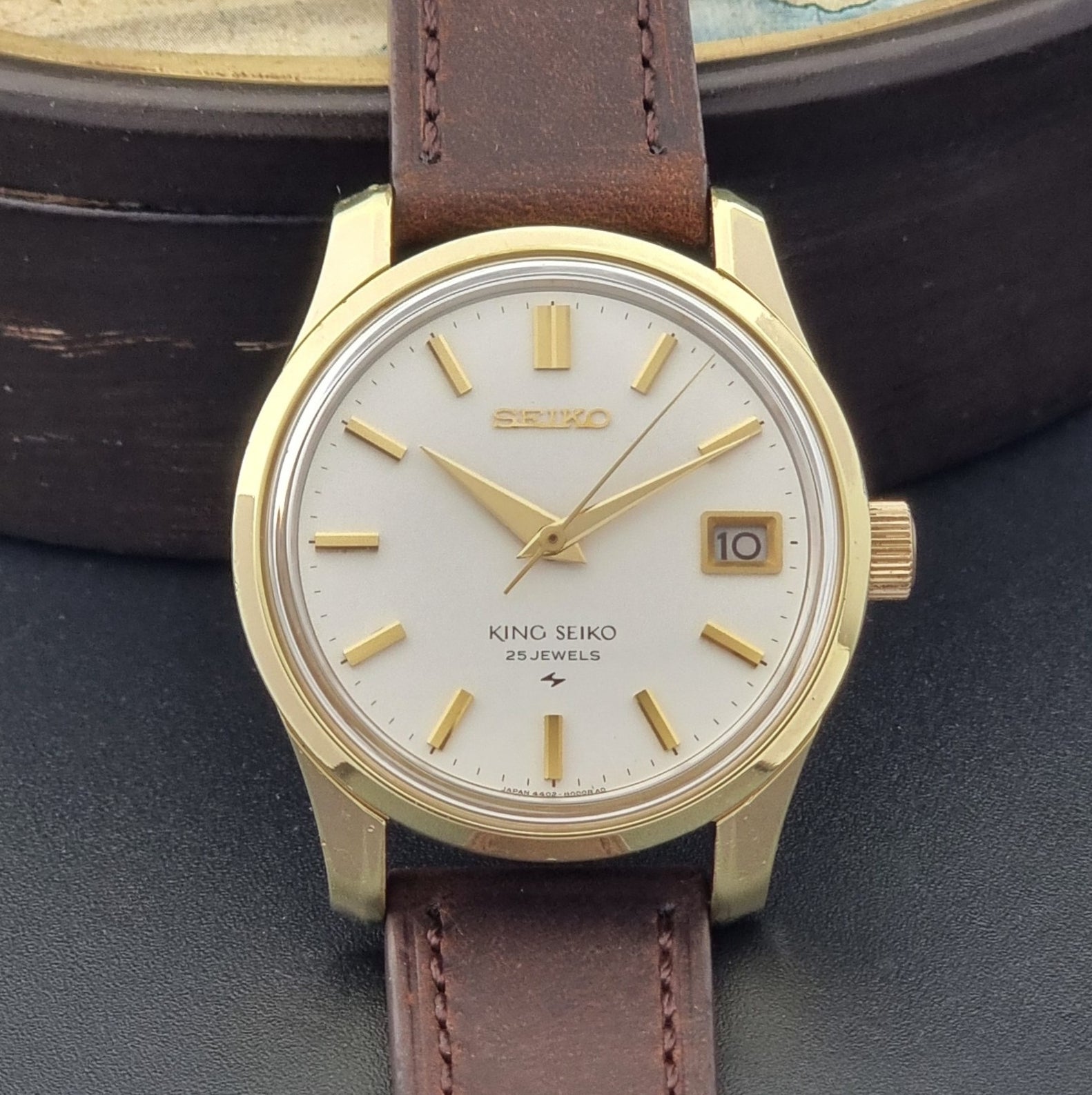 Vintage King Seiko 4402-8000 wristwatch with brown leather strap and gold case on a world map background close up