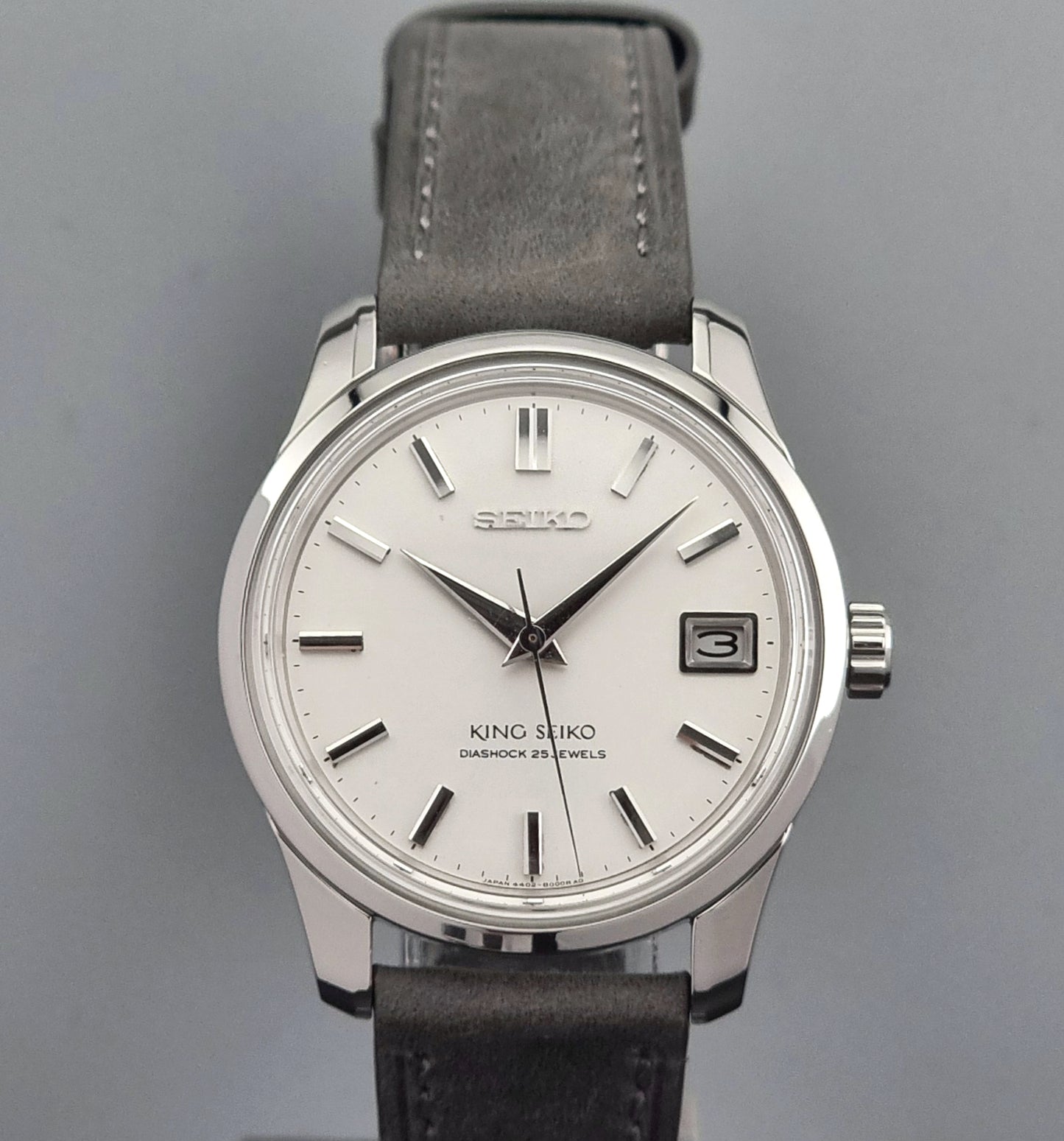 Vintage King Seiko 4402-8000 watch with a silver case and grey leather strap on a gray background close up