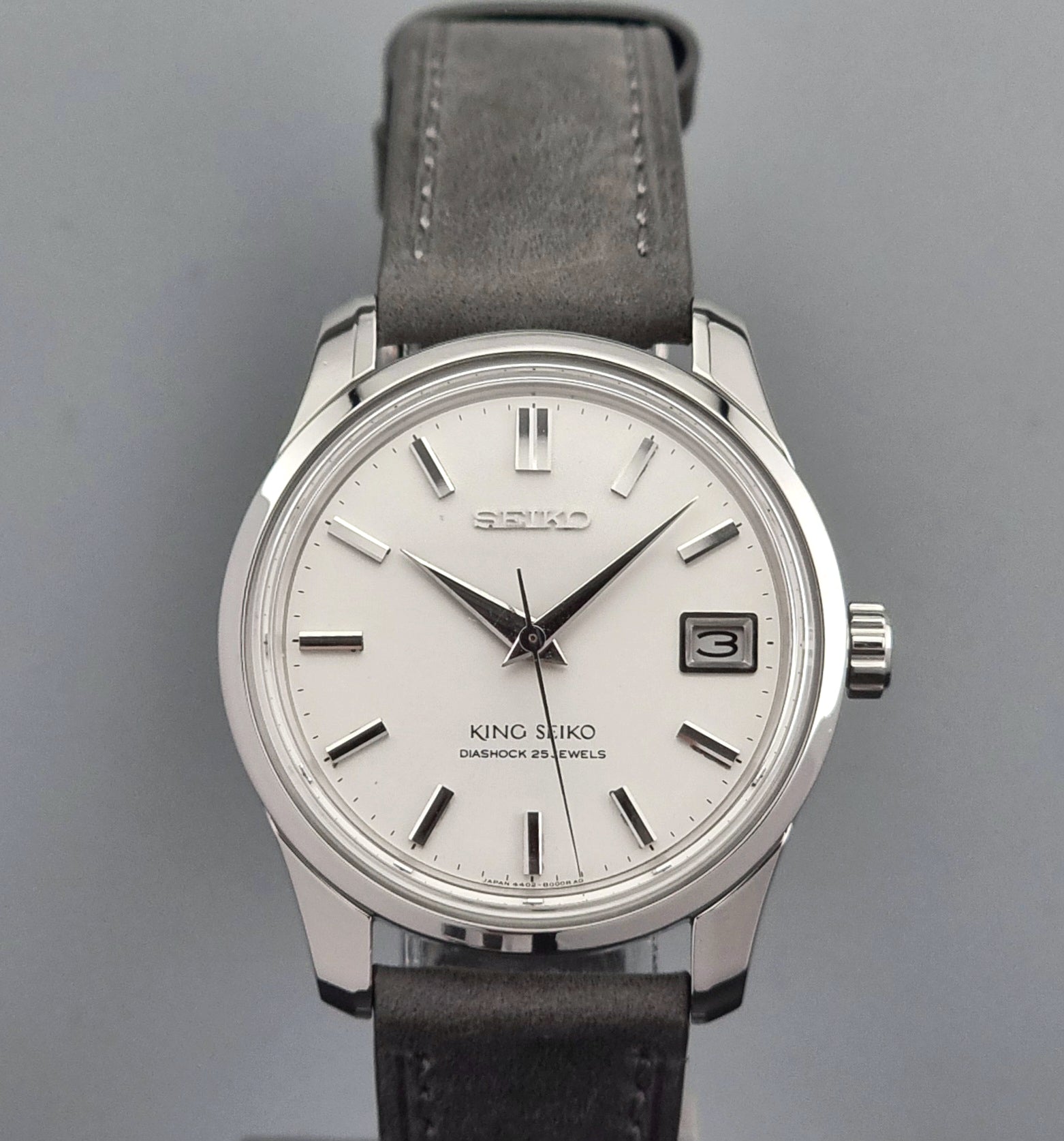 Vintage King Seiko 4402-8000 watch with a silver case and grey leather strap on a gray background close up