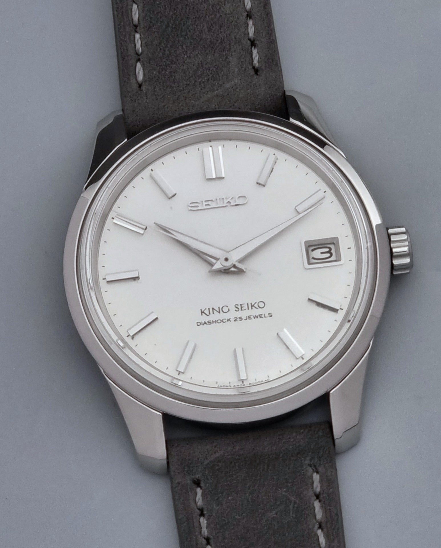 Vintage King Seiko 4402-8000 watch with a silver case and grey leather strap on a gray background close up dial view