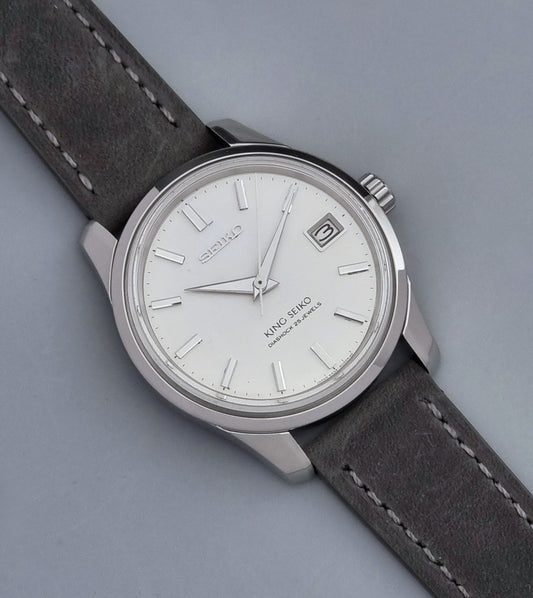 Vintage King Seiko 4402-8000 watch with a silver case and grey leather strap on a gray background front view
