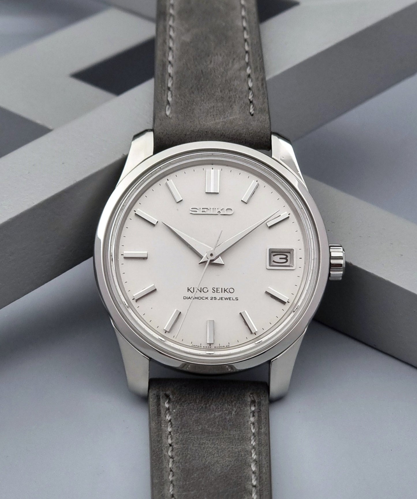 Vintage King Seiko 4402-8000 watch with a silver case and grey leather strap on a gray background