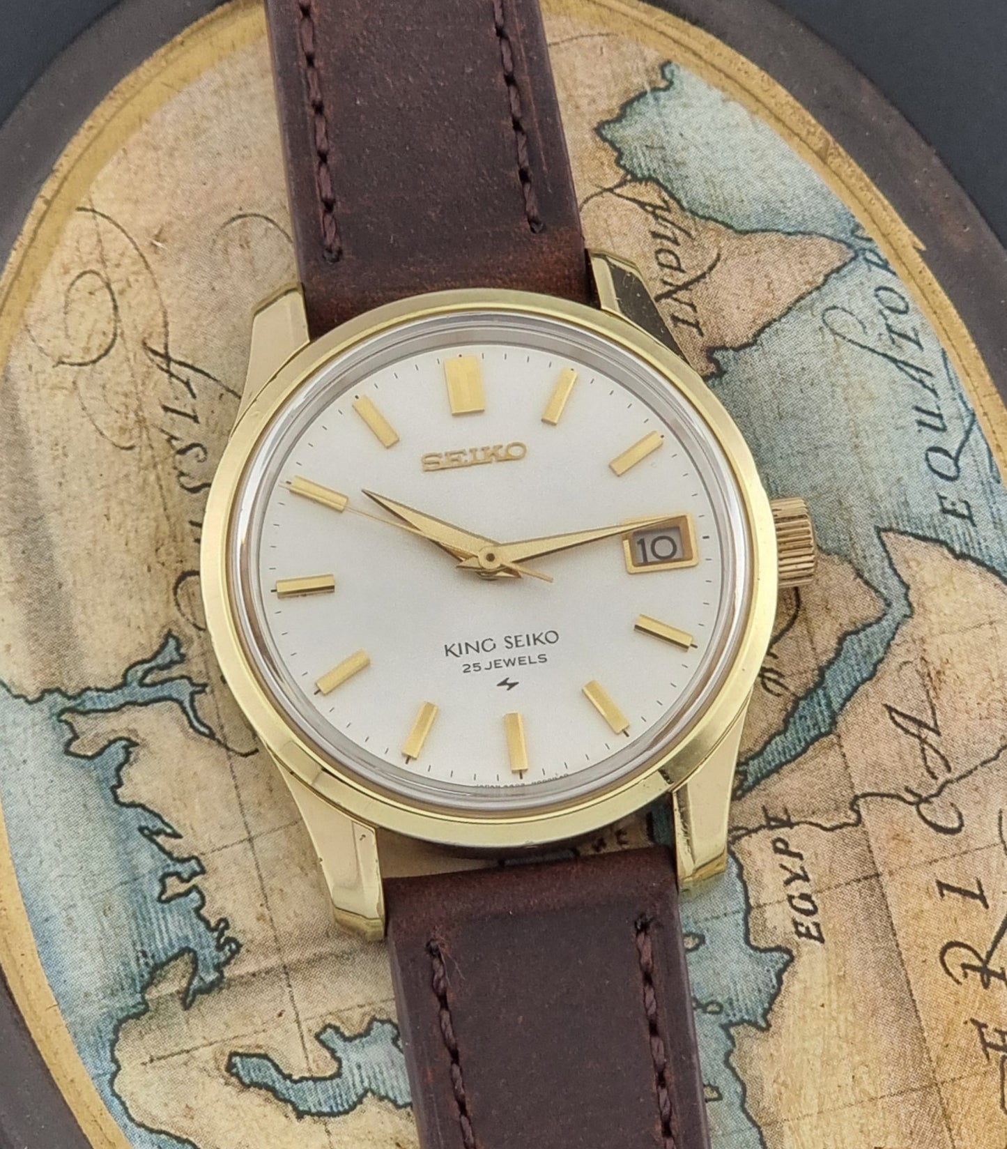 Vintage King Seiko 4402-8000 wristwatch with brown leather strap and gold case on a world map background close up dial view