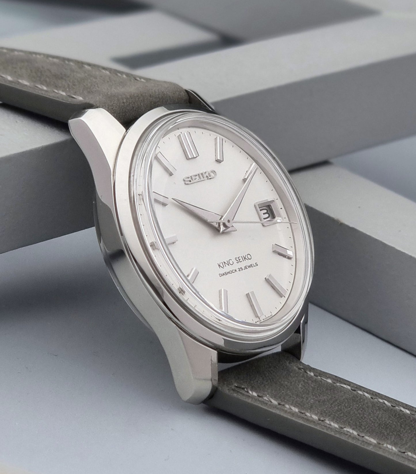 Vintage King Seiko 4402-8000 watch with a silver case and grey leather strap on a gray background side view