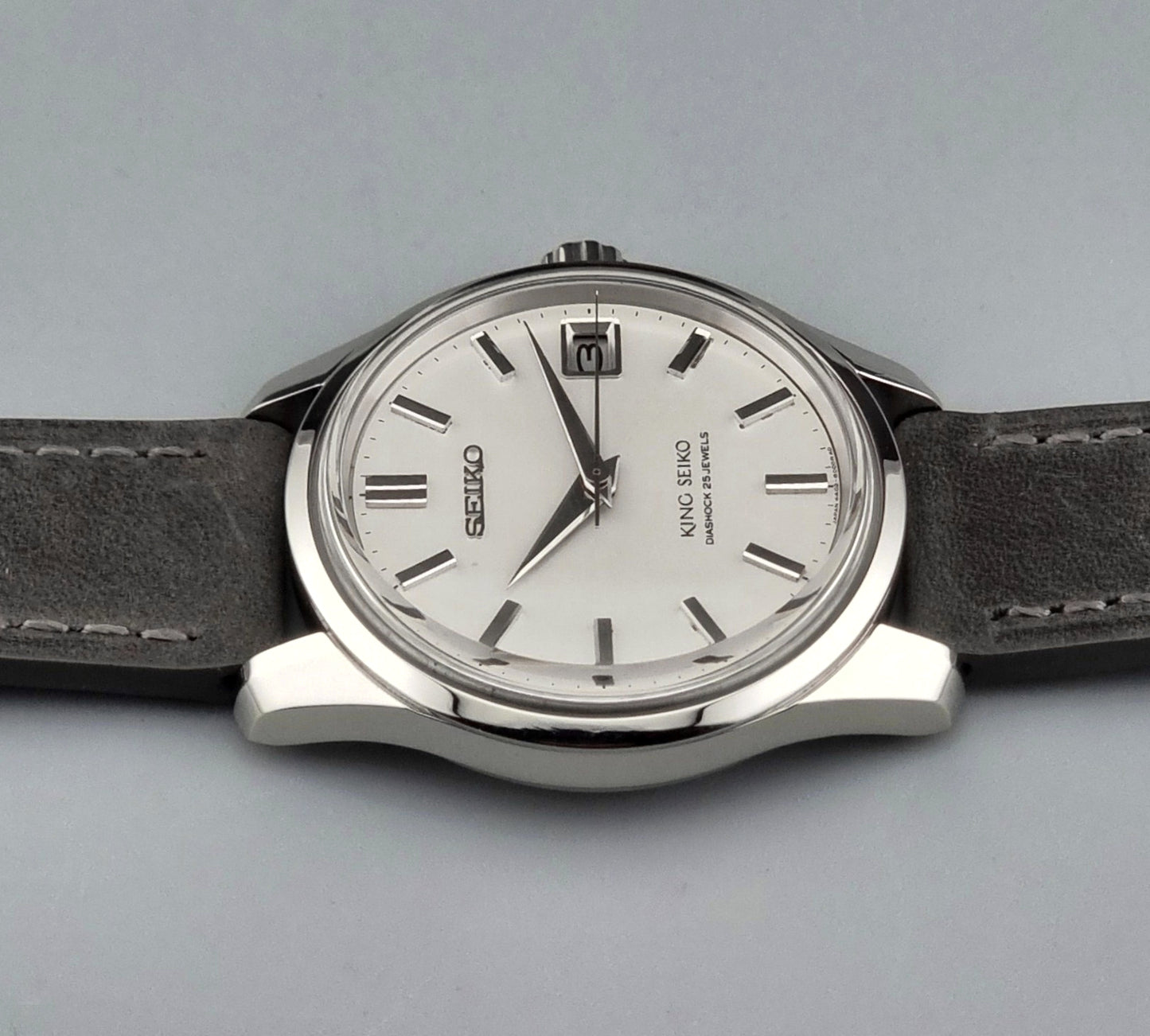 Vintage King Seiko 4402-8000 watch with a silver case and grey leather strap on a gray background angled view side