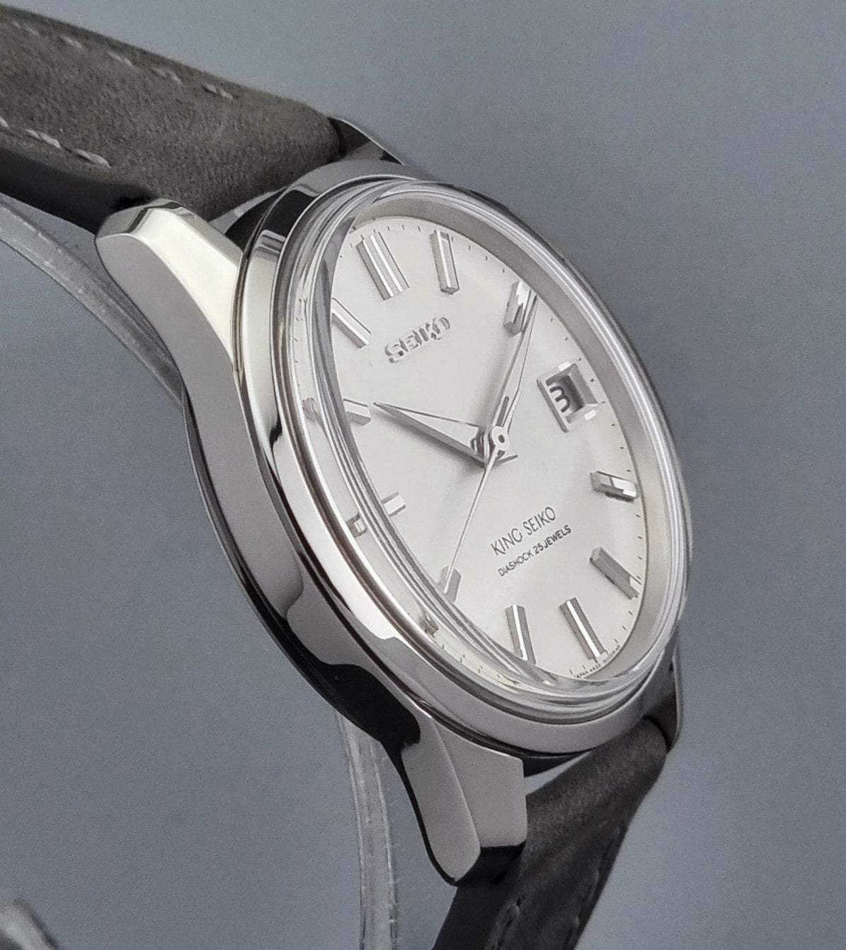 Vintage King Seiko 4402-8000 watch with a silver case and grey leather strap on a gray background side profile close up