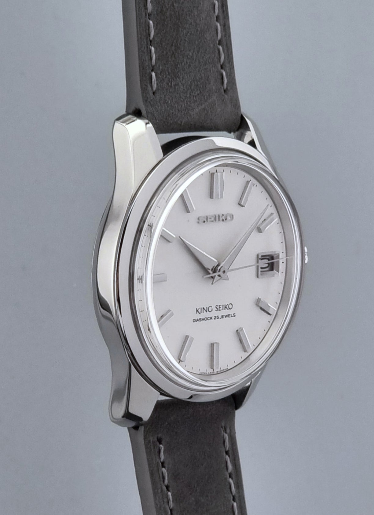 Vintage King Seiko 4402-8000 watch with a silver case and grey leather strap on a gray background side profile