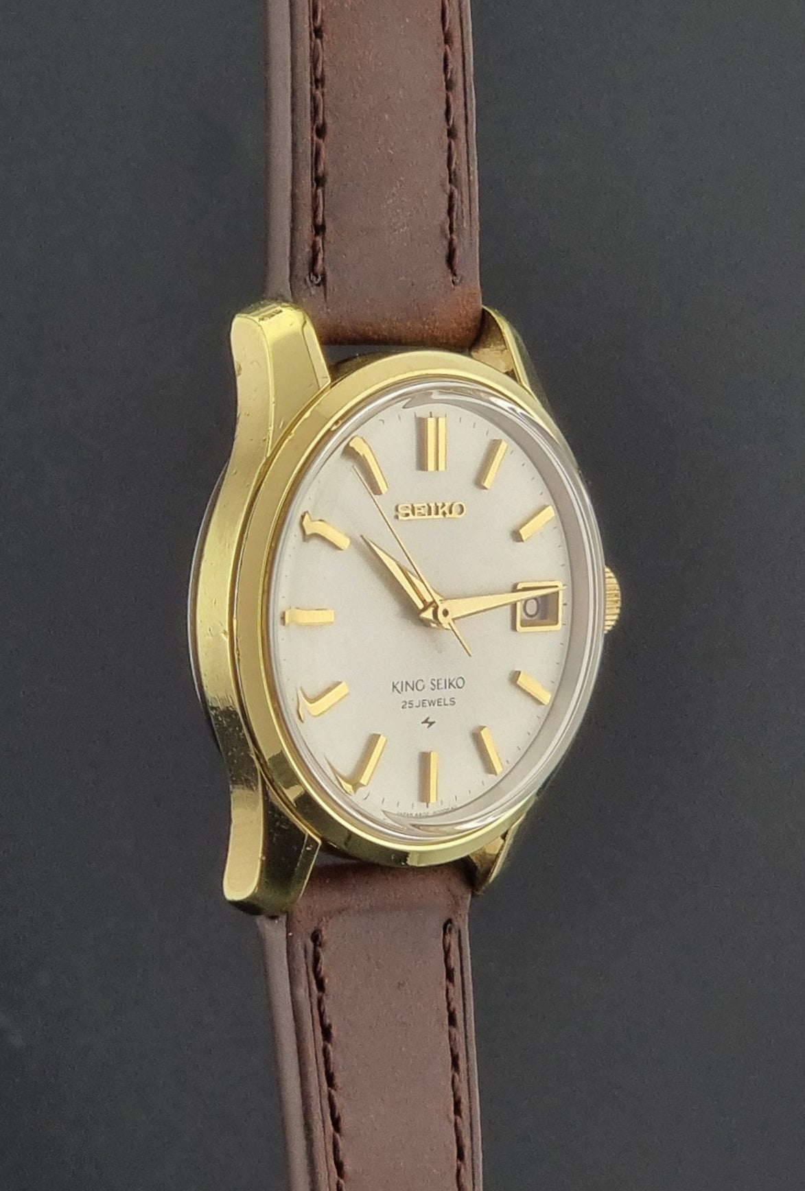Vintage King Seiko 4402-8000 wristwatch with brown leather strap and gold case on a world map background side profile