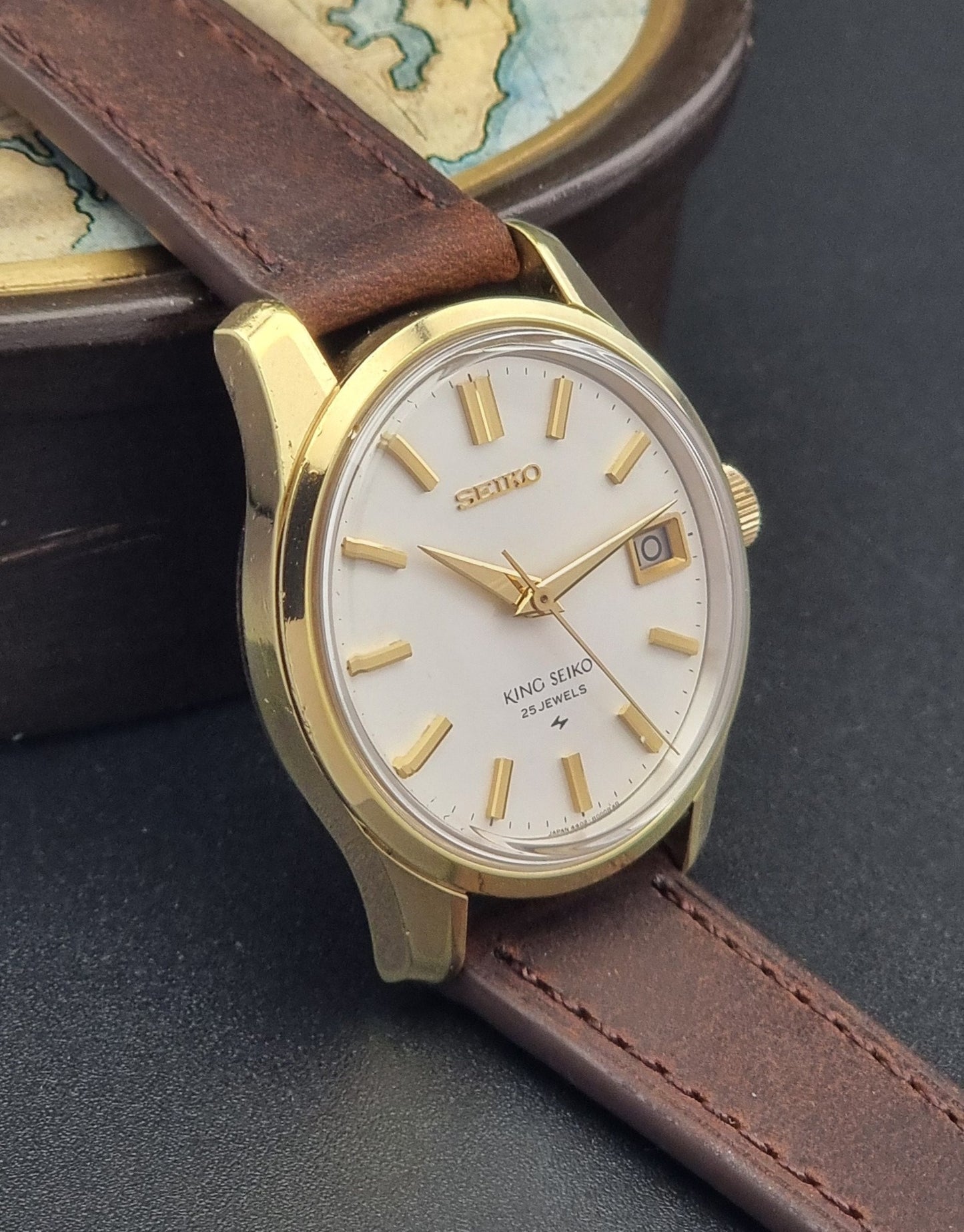 Vintage King Seiko 4402-8000 wristwatch with brown leather strap and gold case on a world map background side view