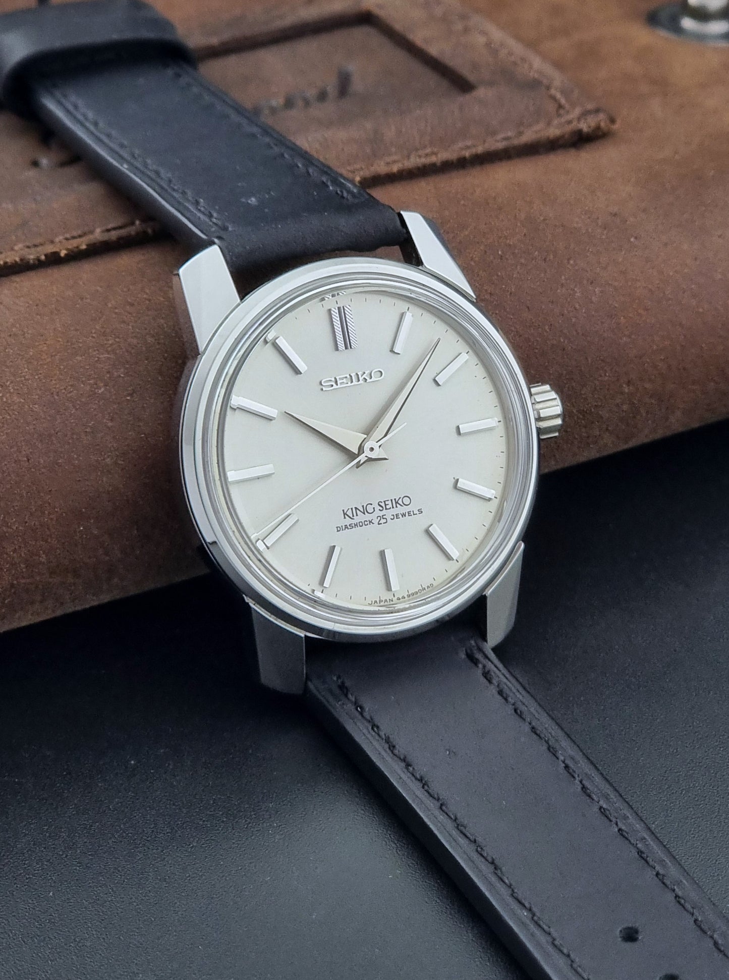Vintage King Seiko Wristwatch 44999  with a black leather strap on a dark surface side view