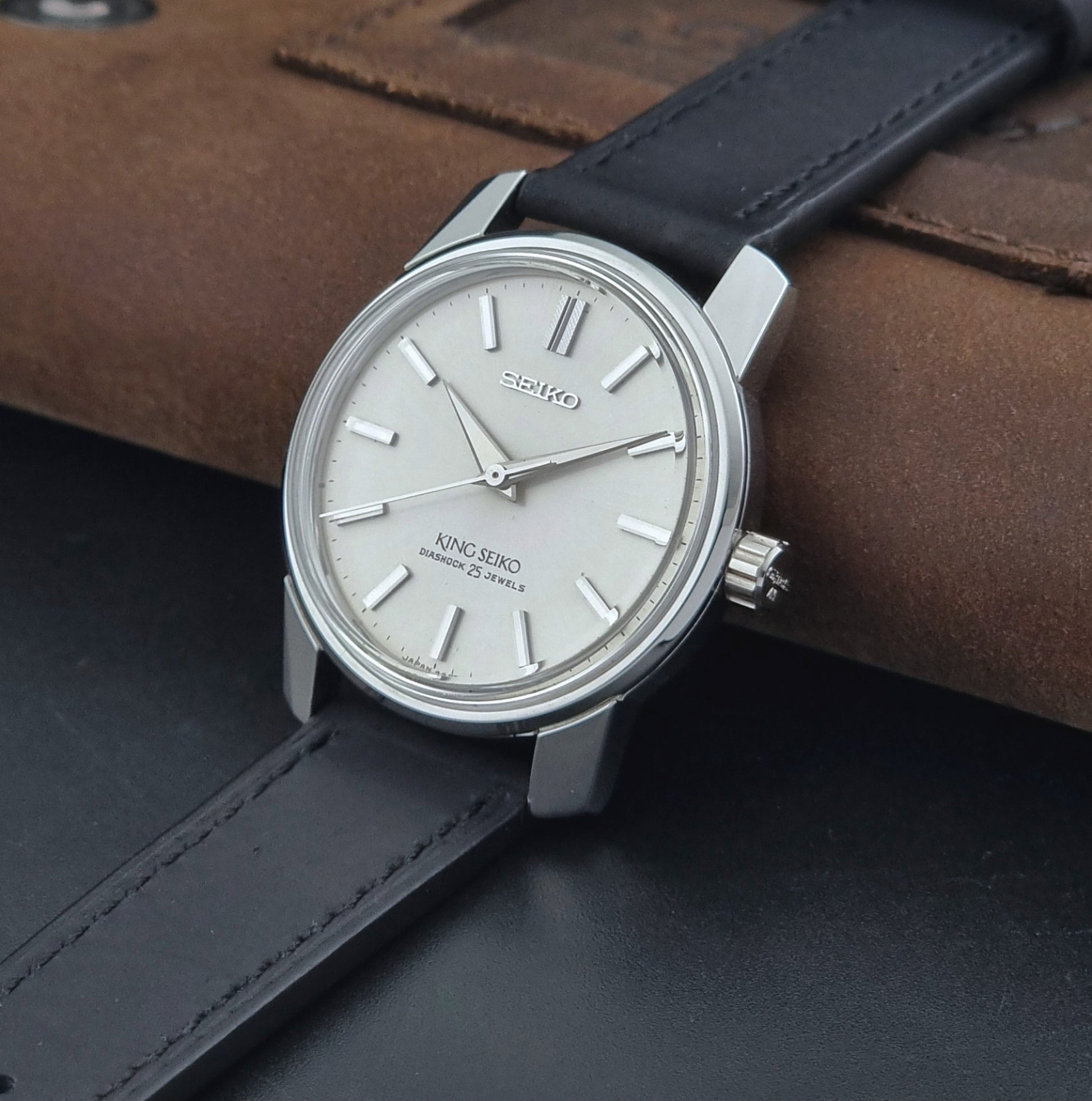 Vintage King Seiko Wristwatch 44999  with a black leather strap on a dark surface crown view