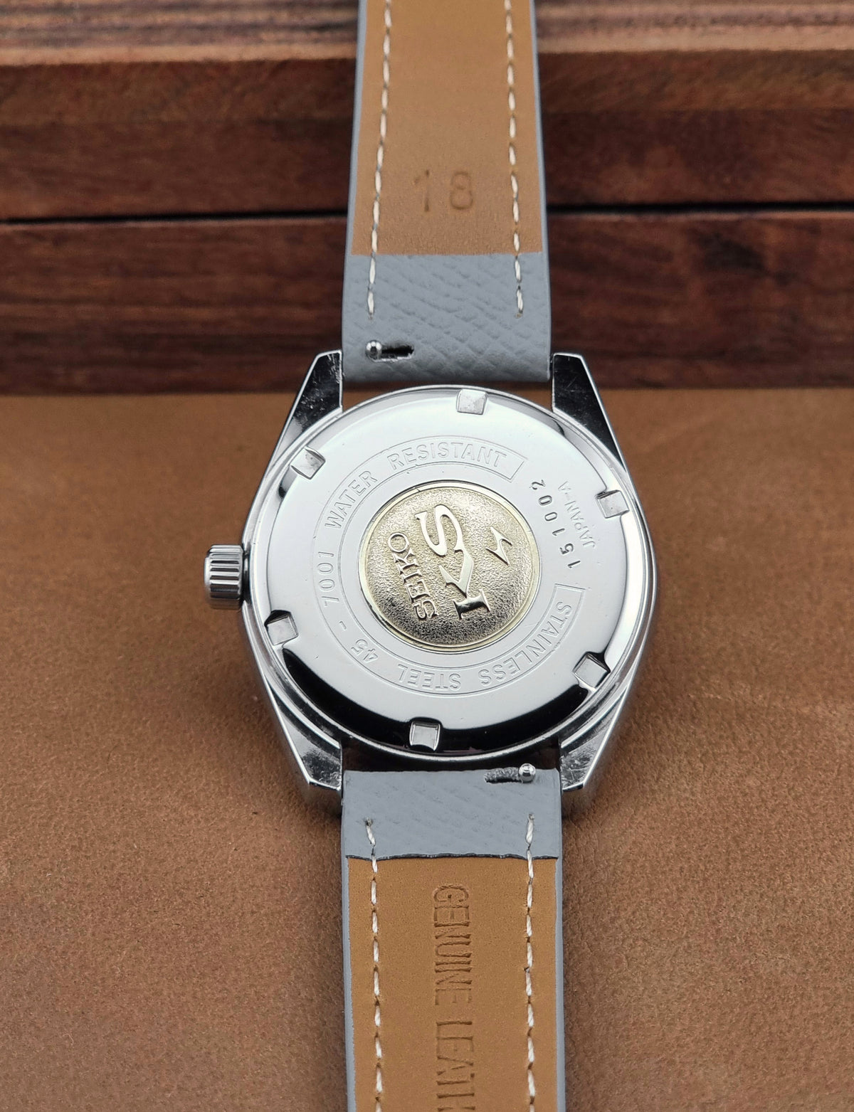Vintage King Seiko 45-7001 watch with a grey leather strap on a brown background case back view