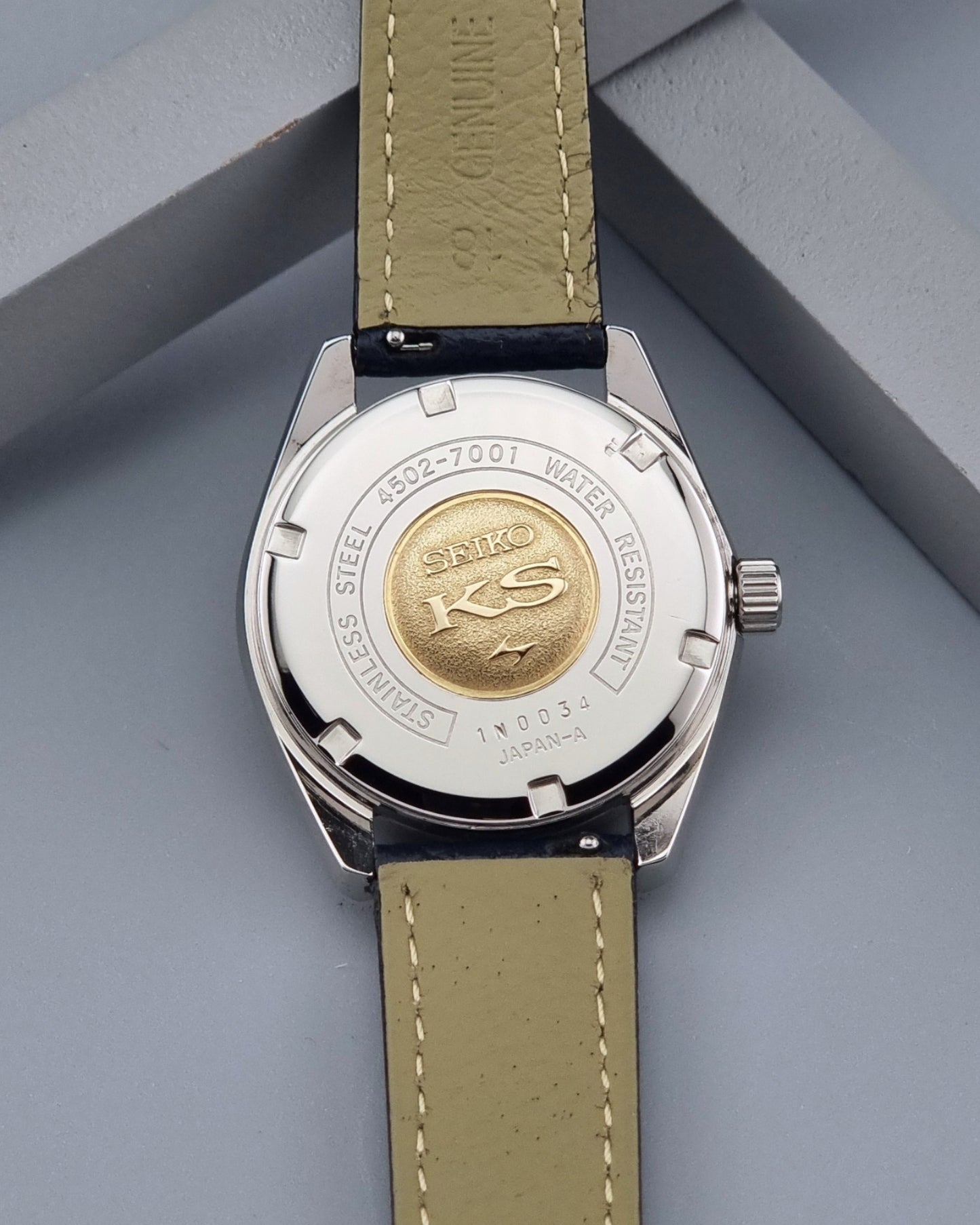 Vintage King Seiko 4502-7001 watch with a blue leather strap on a grey back ground case back view