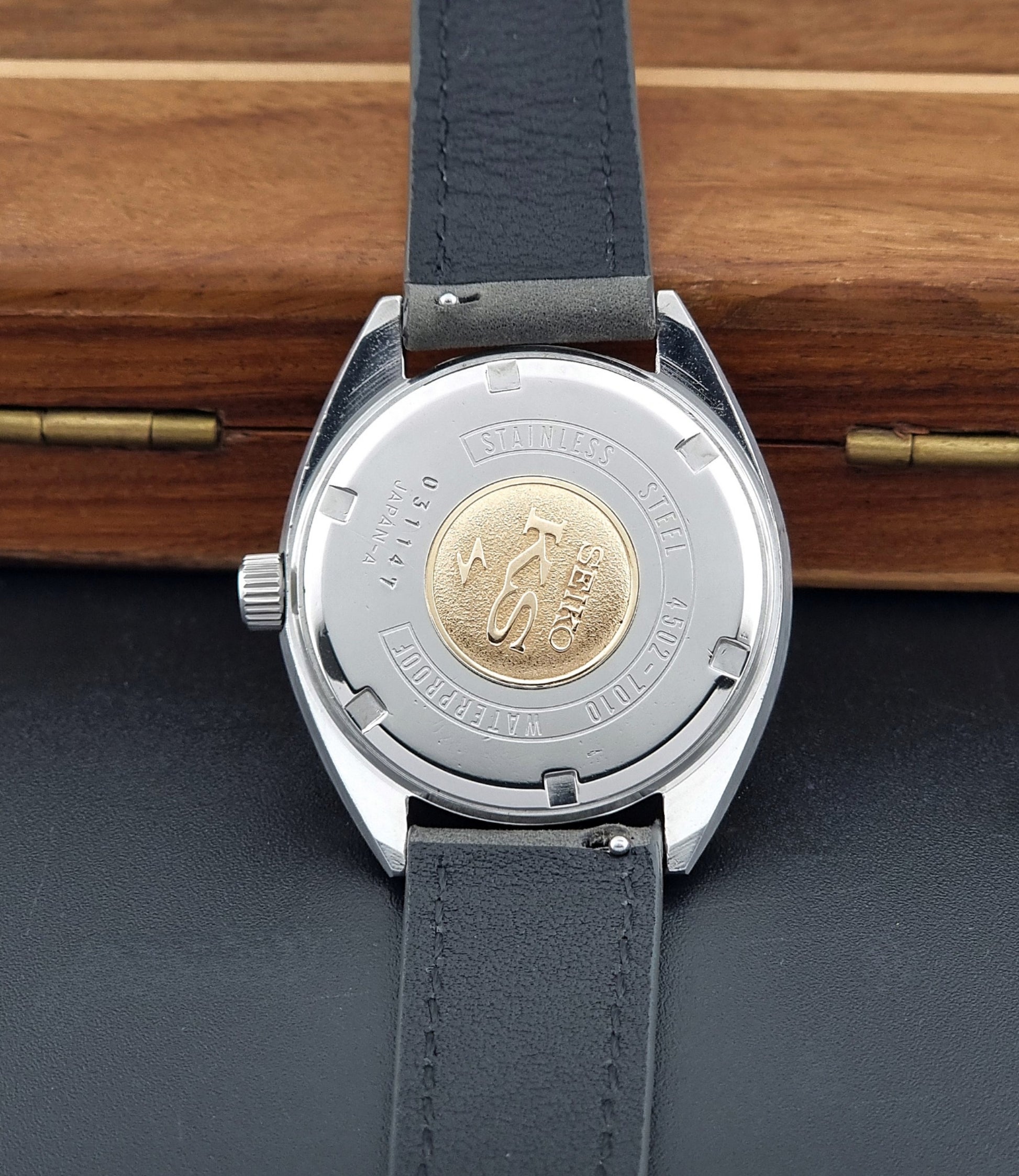 Vintage King Seiko Wristwatch 4502-7010 with gray strap and silver case on a wooden surface case back view