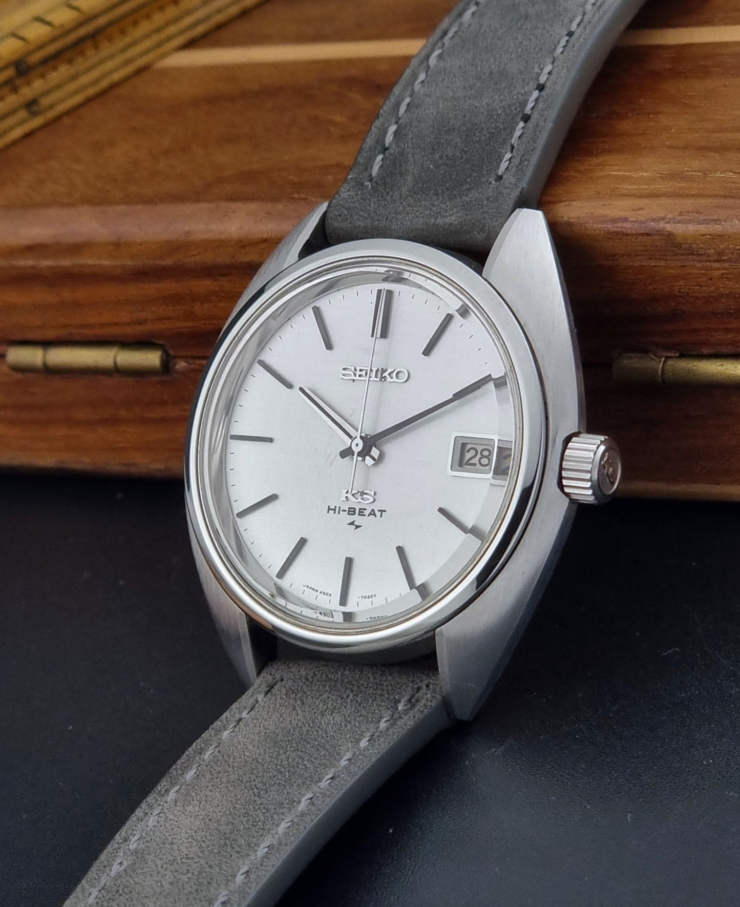 Vintage King Seiko Wristwatch 4502-7010 with gray strap and silver case on a wooden surface crown view
