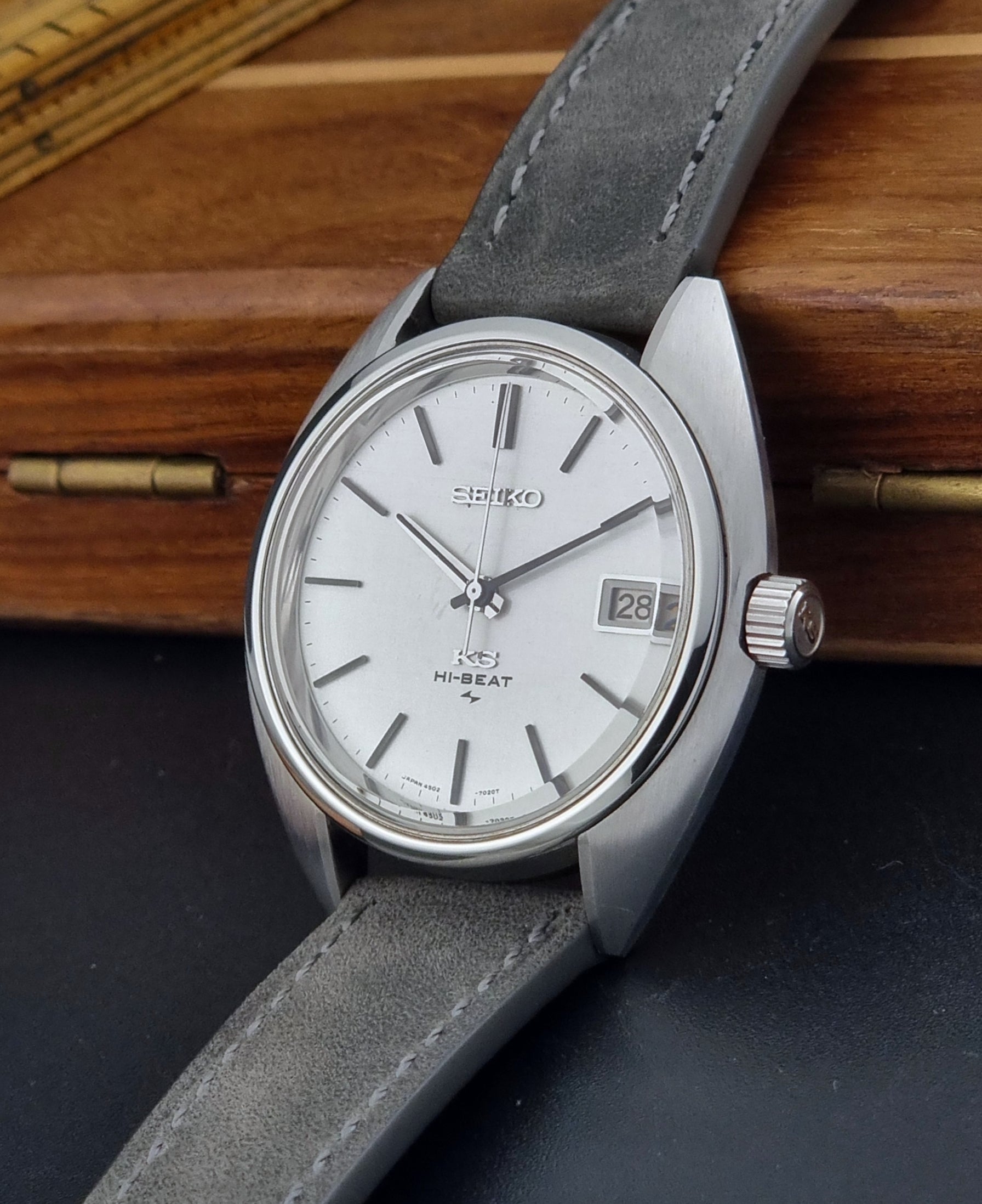 Vintage King Seiko Wristwatch 4502-7010 with gray strap and silver case on a wooden surface crown view