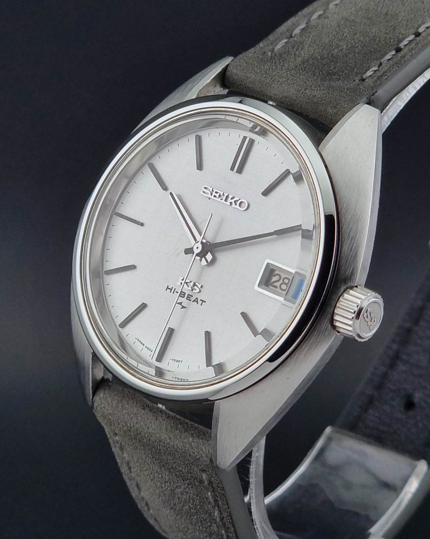 Vintage King Seiko Wristwatch 4502-7010 with gray strap and silver case on a dark surface close crown profile view
