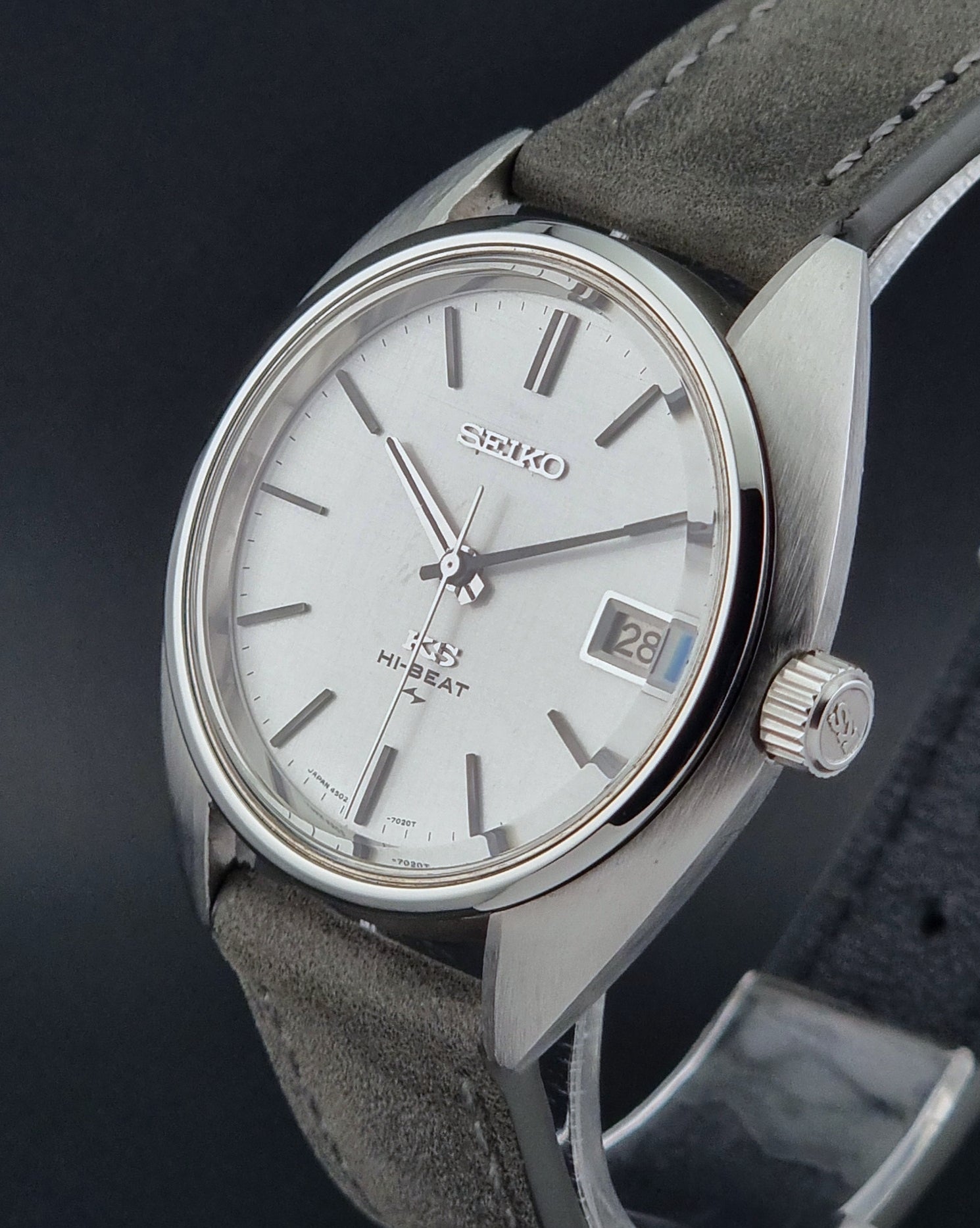 Vintage King Seiko Wristwatch 4502-7010 with gray strap and silver case on a dark surface close crown profile view