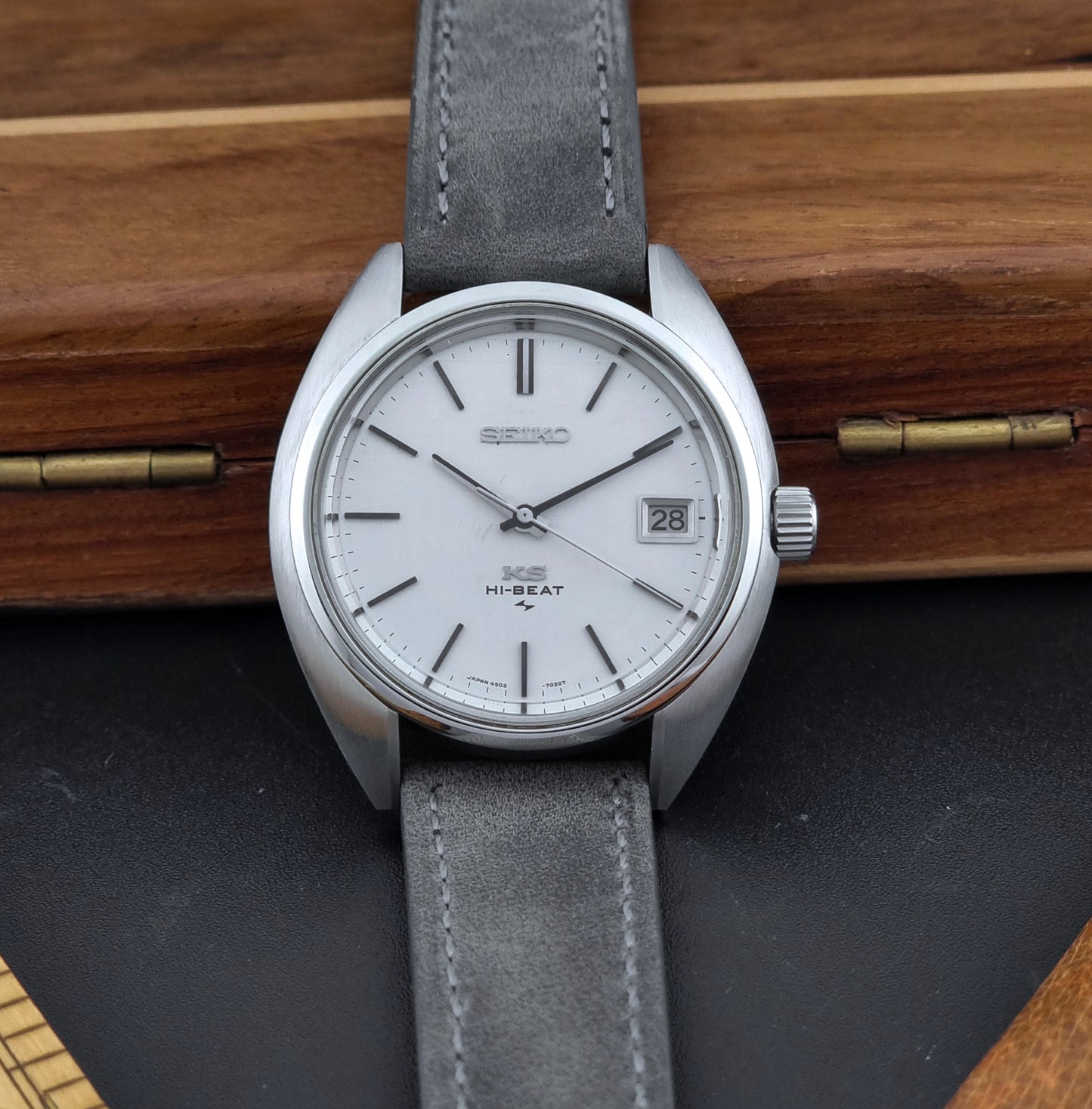 Vintage King Seiko Wristwatch 4502-7010 with gray strap and silver case on a wooden surface front view