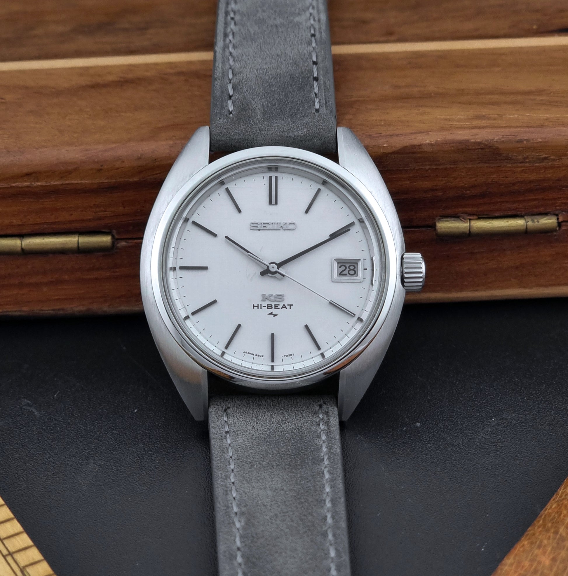 Vintage King Seiko Wristwatch 4502-7010 with gray strap and silver case on a wooden surface front view