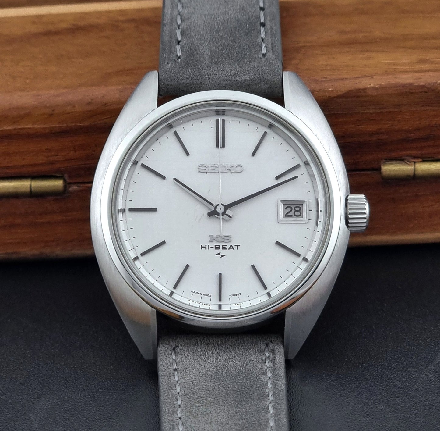 Vintage King Seiko Wristwatch 4502-7010 with gray strap and silver case on a wooden surface dial view