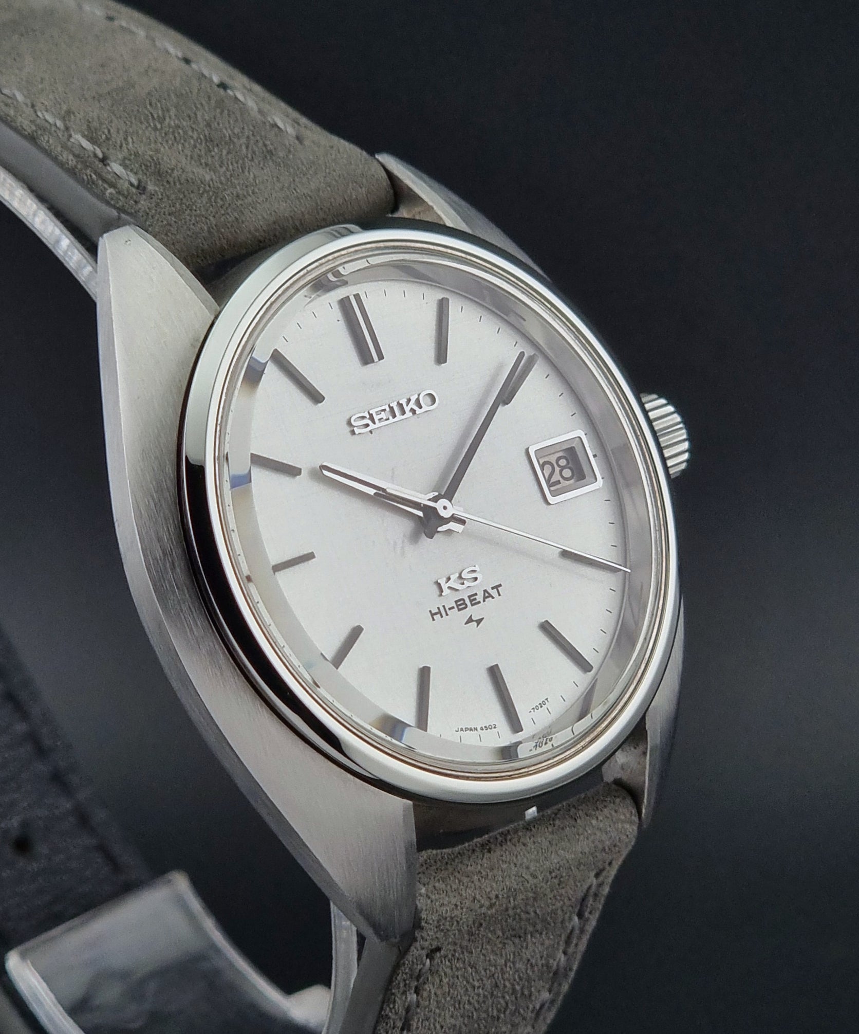 Vintage King Seiko Wristwatch 4502-7010 with gray strap and silver case on a dark surface close side profile view