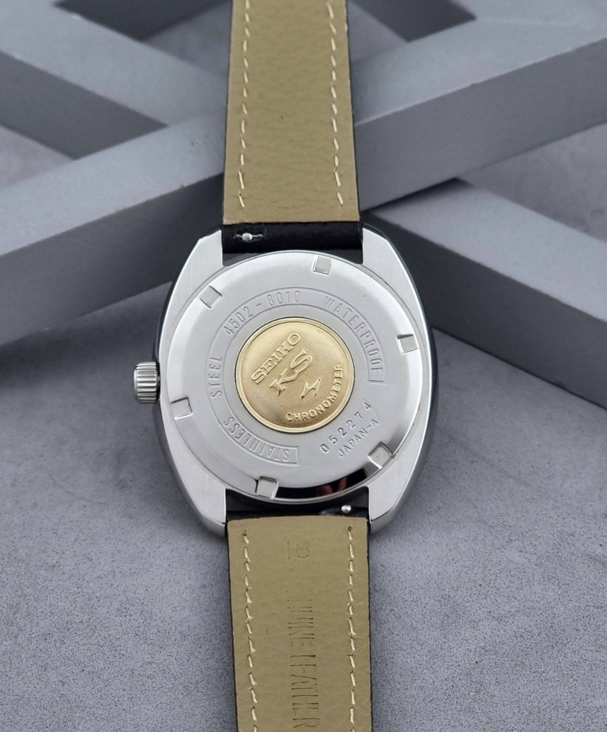 Vintage King Seiko Wristwatch 4502-8010 with black leather strap on a gray background case back view