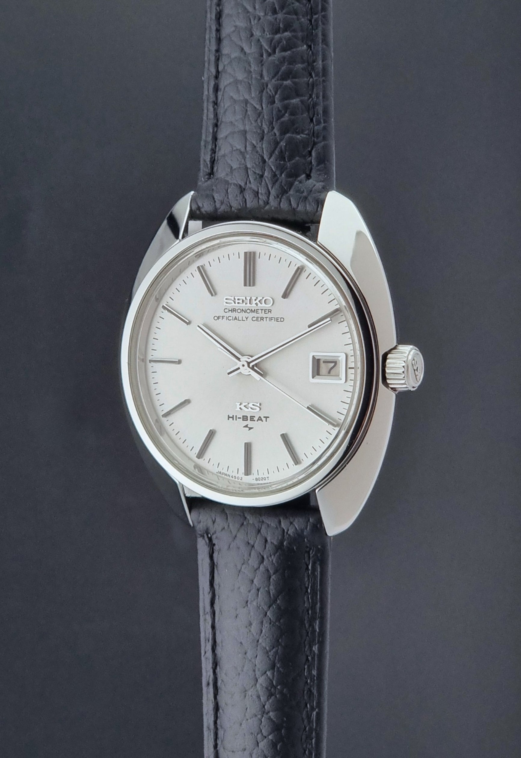 Vintage King Seiko Wristwatch 4502-8010 with black leather strap on a gray background crown profle view