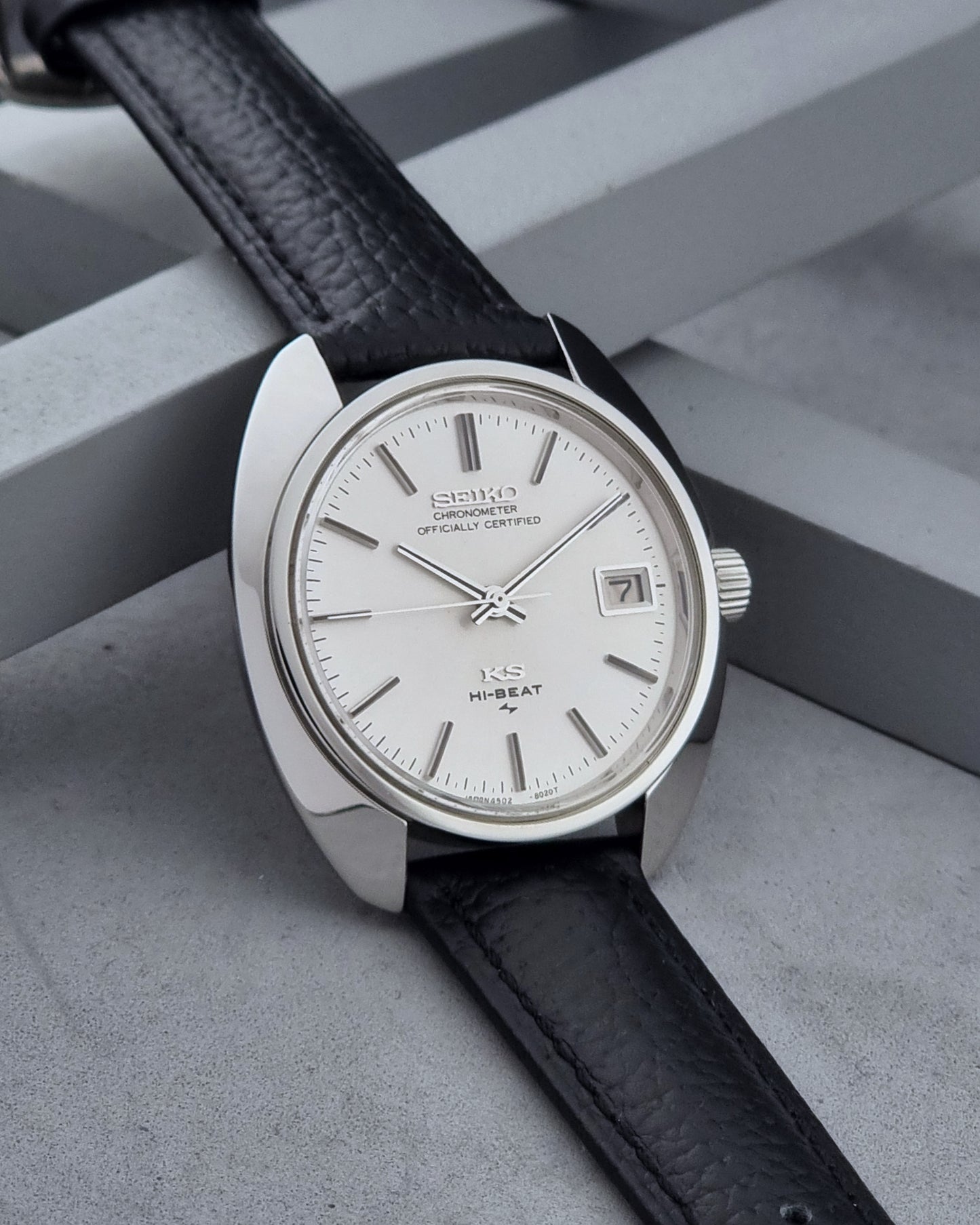 Vintage King Seiko Wristwatch 4502-8010 with black leather strap on a gray background side view