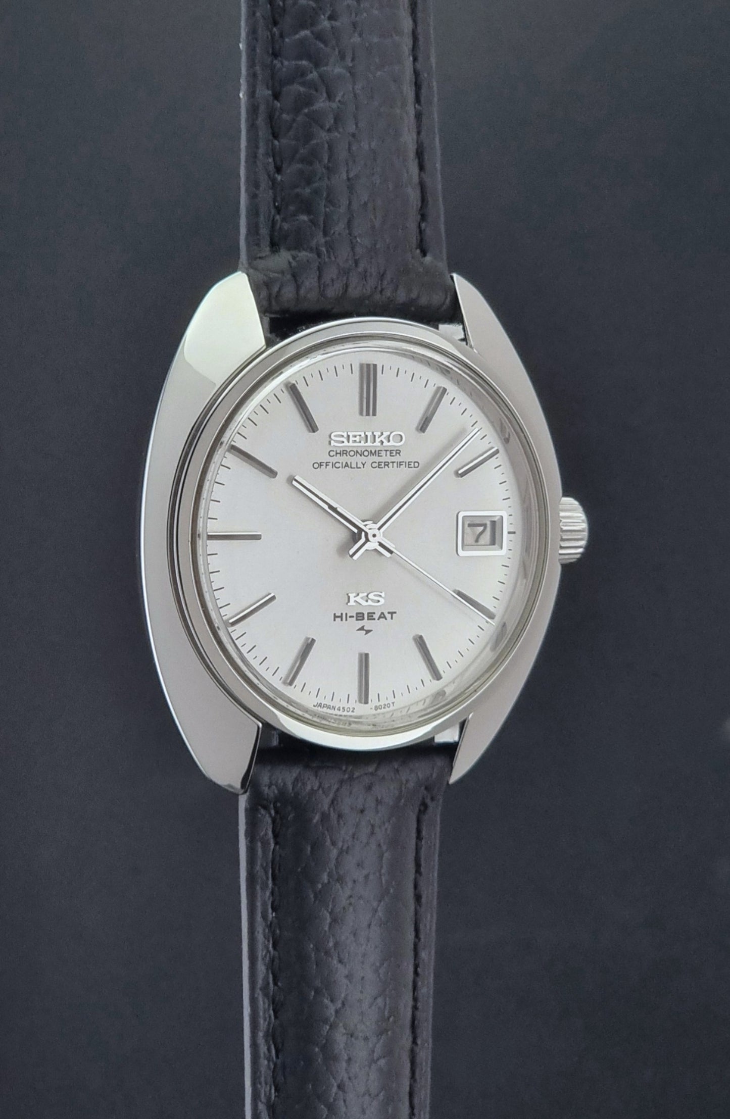 Vintage King Seiko Wristwatch 4502-8010 with black leather strap on a gray background side profile view