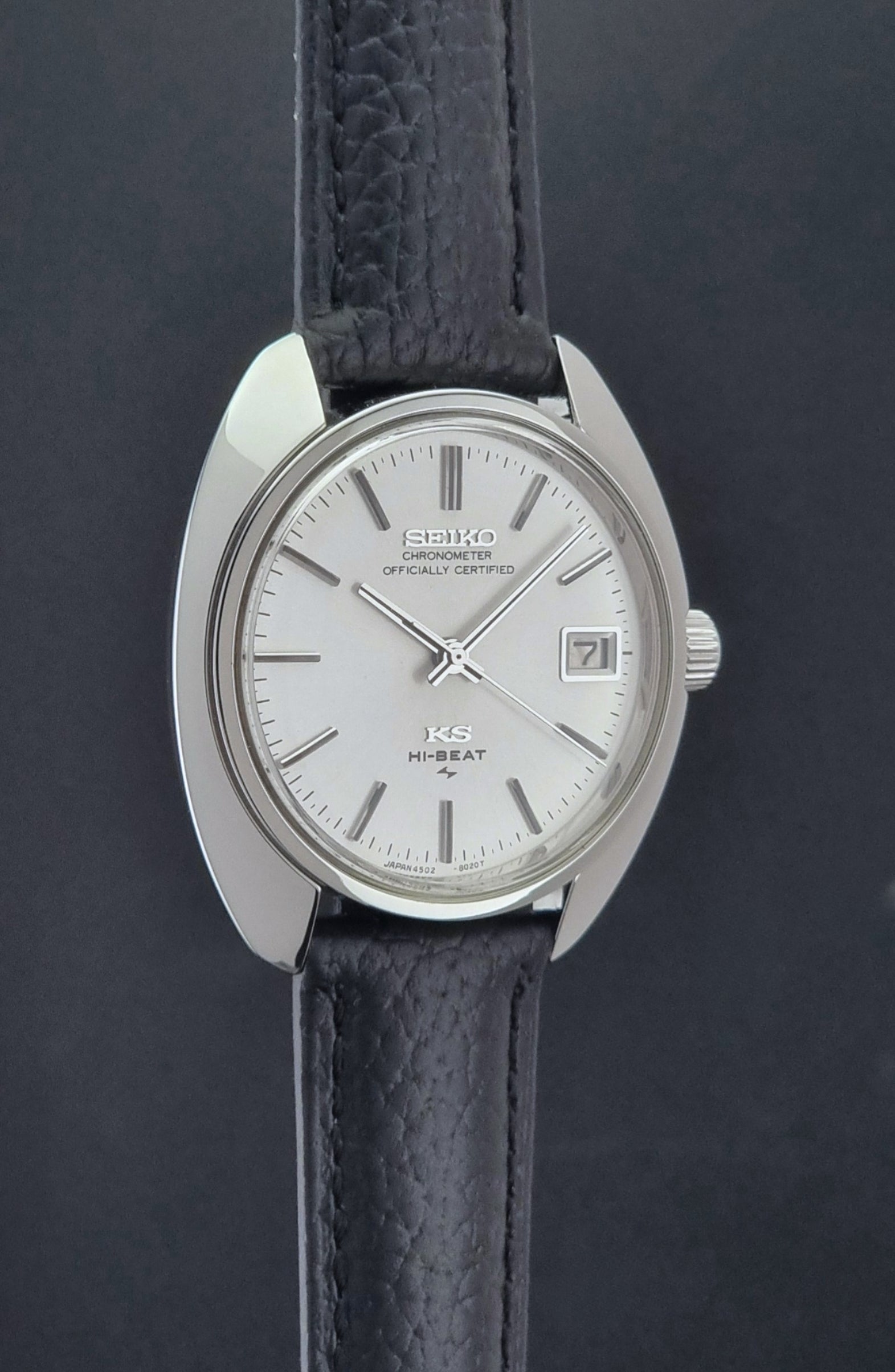 Vintage King Seiko Wristwatch 4502-8010 with black leather strap on a gray background side profile view