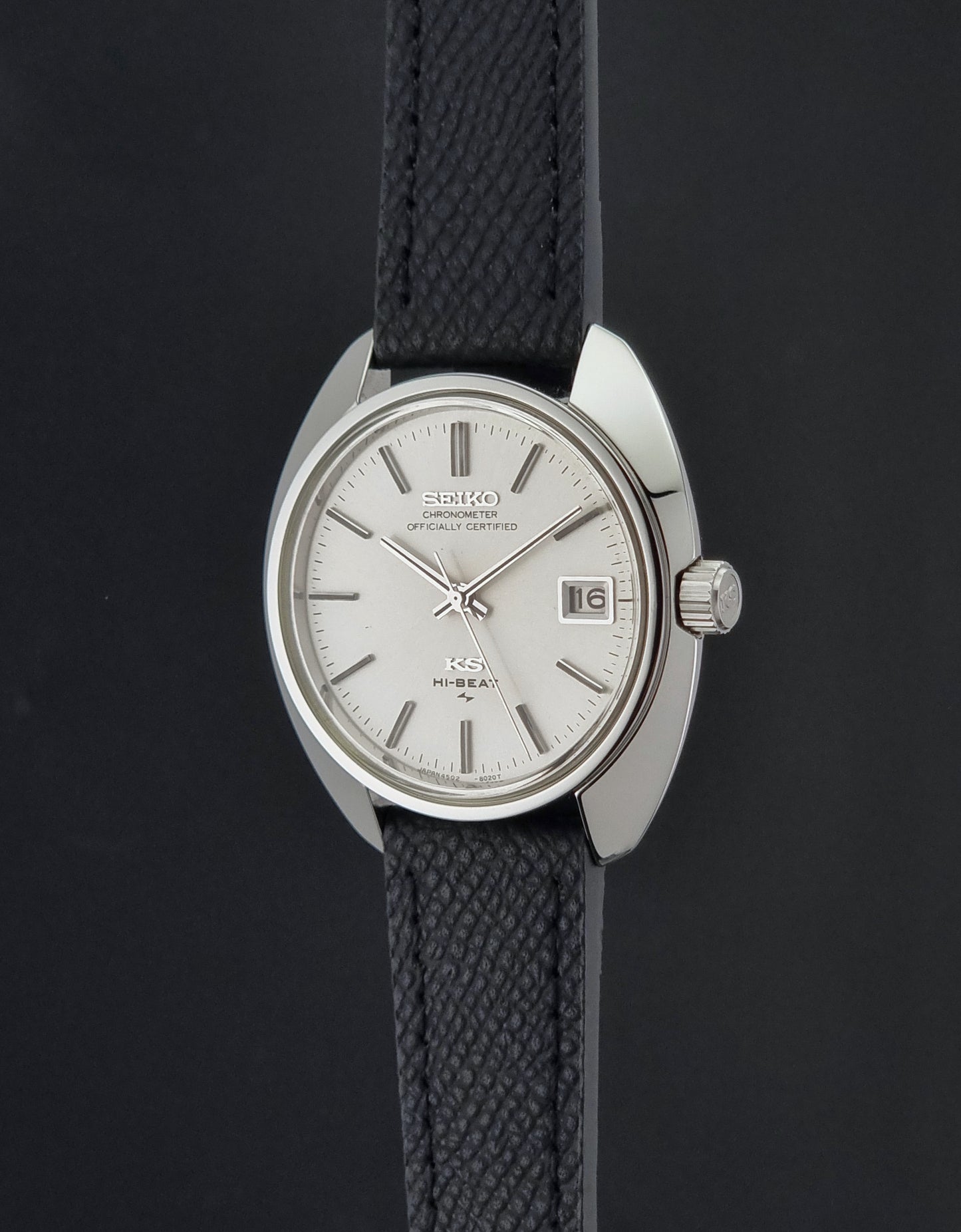 Vintage King Seiko Wristwatch 4502-8010 with a silver-toned metal case, white dial, and black textured leather strap, on a dark background side profile view