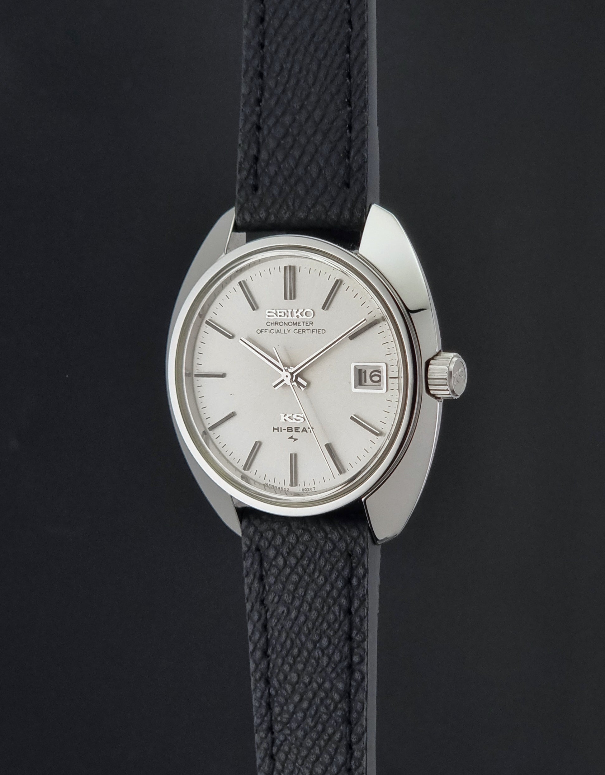 Vintage King Seiko Wristwatch 4502-8010 with a silver-toned metal case, white dial, and black textured leather strap, on a dark background side profile view
