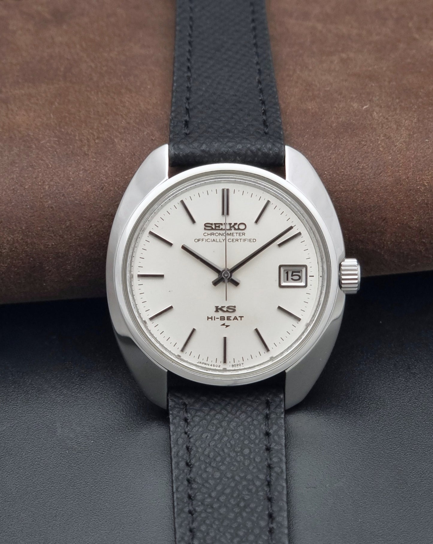 Vintage King Seiko Wristwatch 4502-8010 with a silver-toned metal case, white dial, and black textured leather strap, on a dark background dial view
