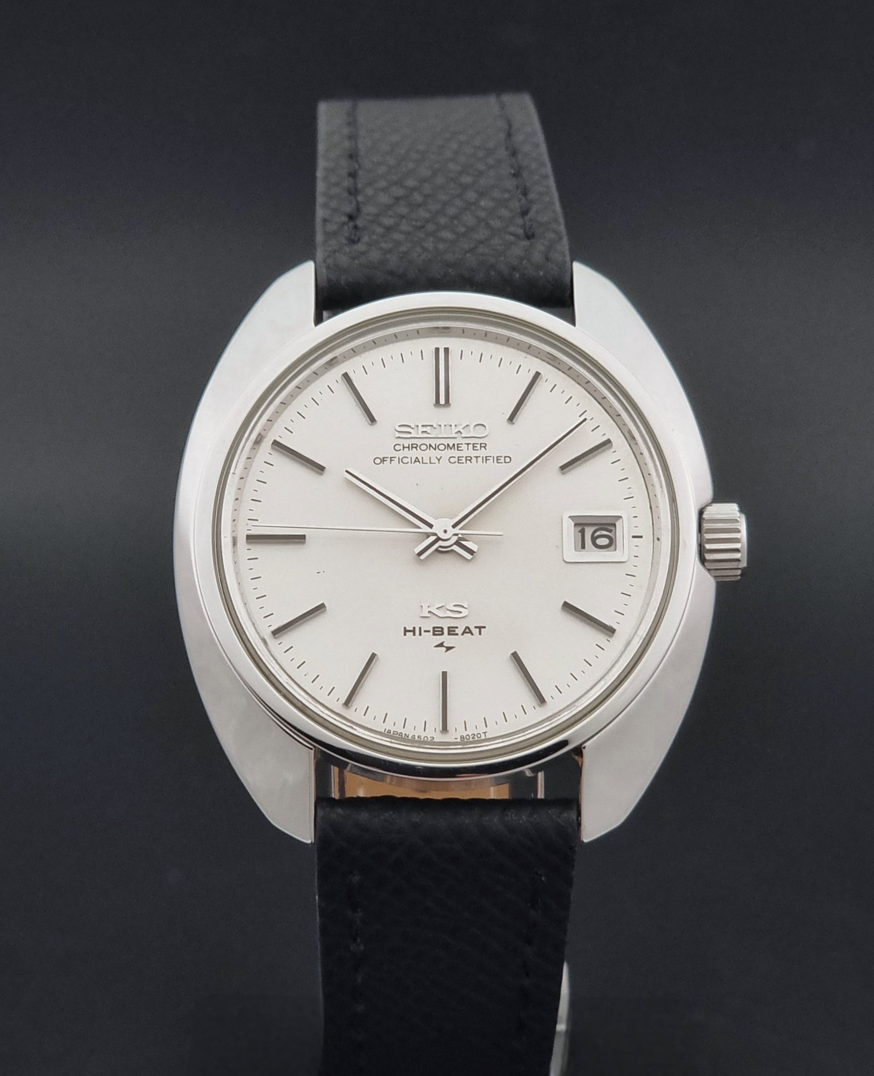 Vintage King Seiko Wristwatch 4502-8010 with a silver-toned metal case, white dial, and black textured leather strap, on a dark background close dial view