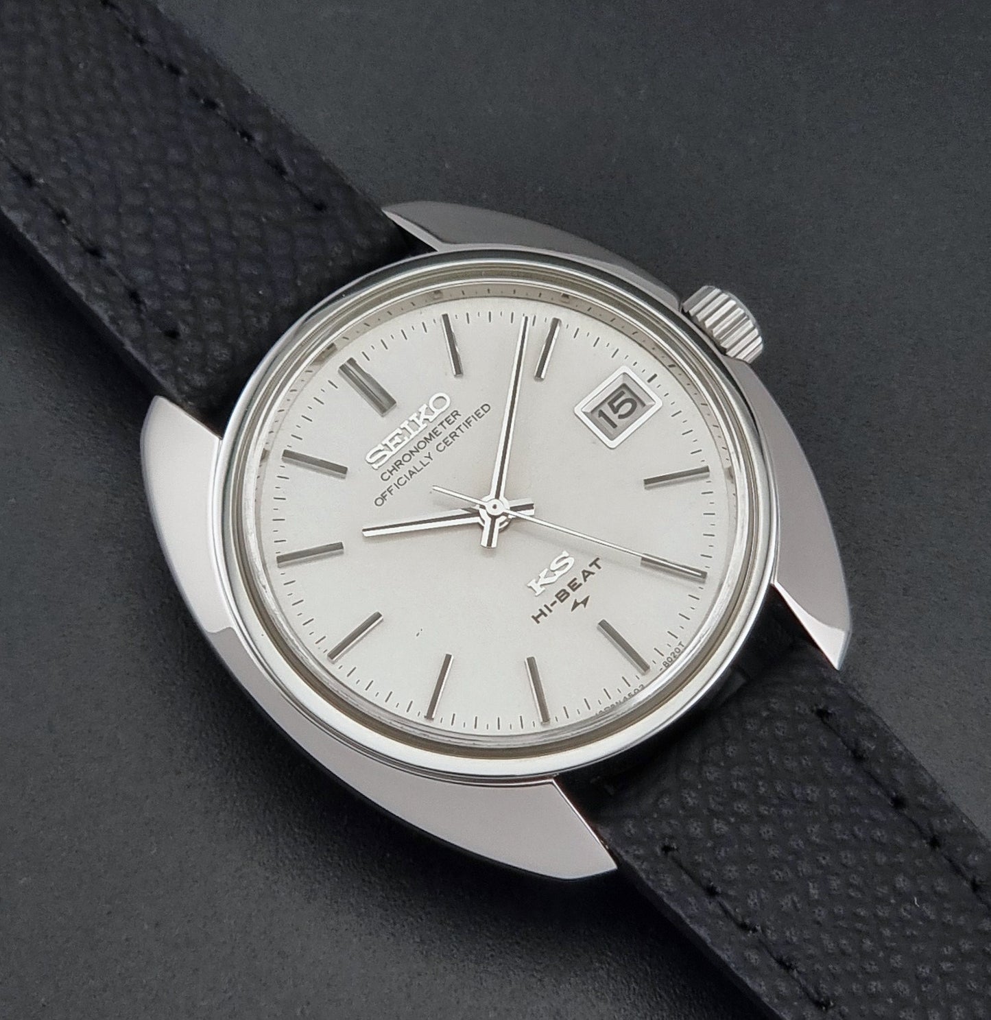 Vintage King Seiko Wristwatch 4502-8010 with a silver-toned metal case, white dial, and black textured leather strap, on a dark background close up dial view