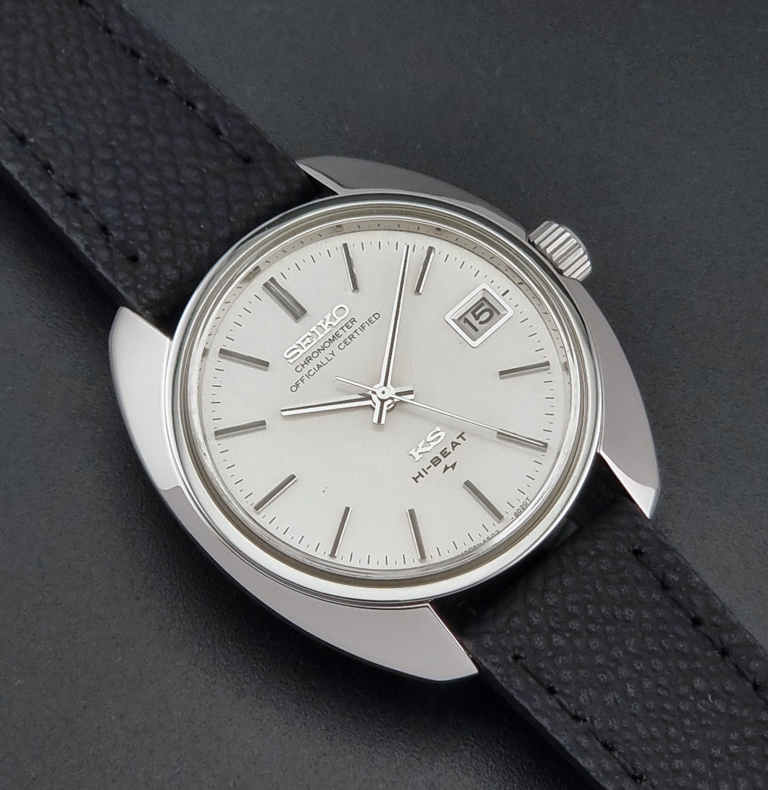 Vintage King Seiko Wristwatch 4502-8010 with a silver-toned metal case, white dial, and black textured leather strap, on a dark background close up dial view