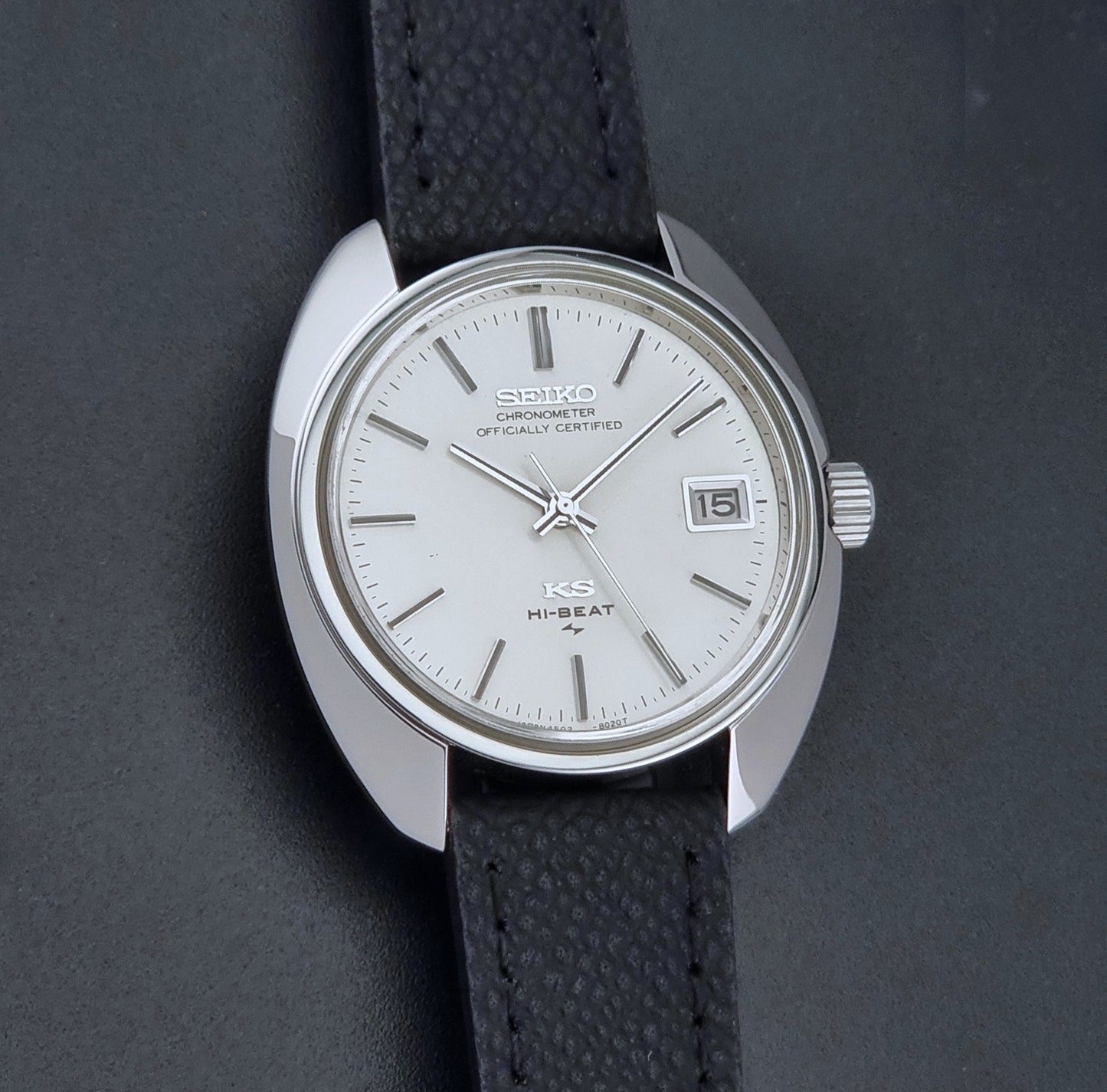 Vintage King Seiko Wristwatch 4502-8010 with a silver-toned metal case, white dial, and black textured leather strap, on a dark background front view