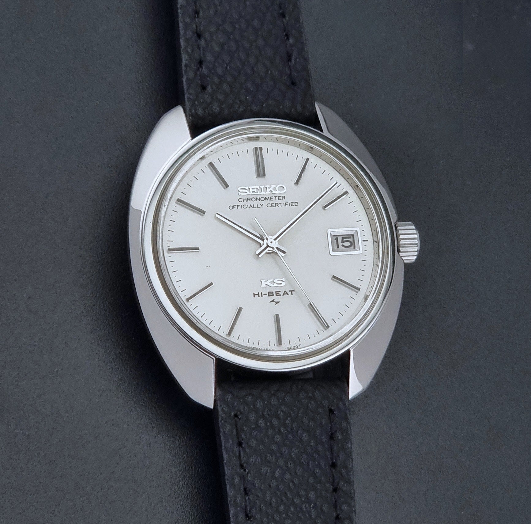 Vintage King Seiko Wristwatch 4502-8010 with a silver-toned metal case, white dial, and black textured leather strap, on a dark background front view